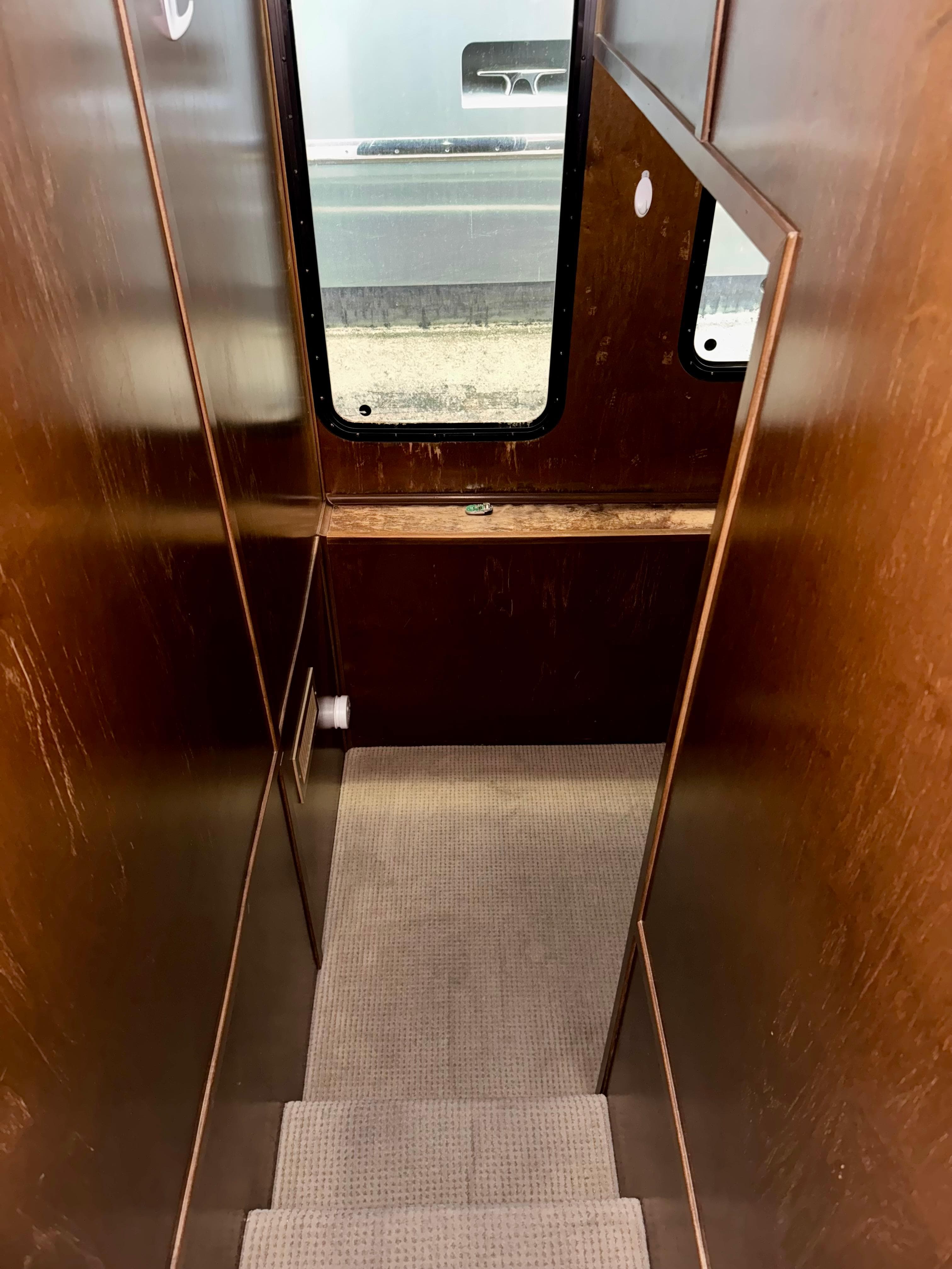Narrow wooden staircase with carpet, leading to a window in a 2013 Bravada Bella Luna Trip #16.