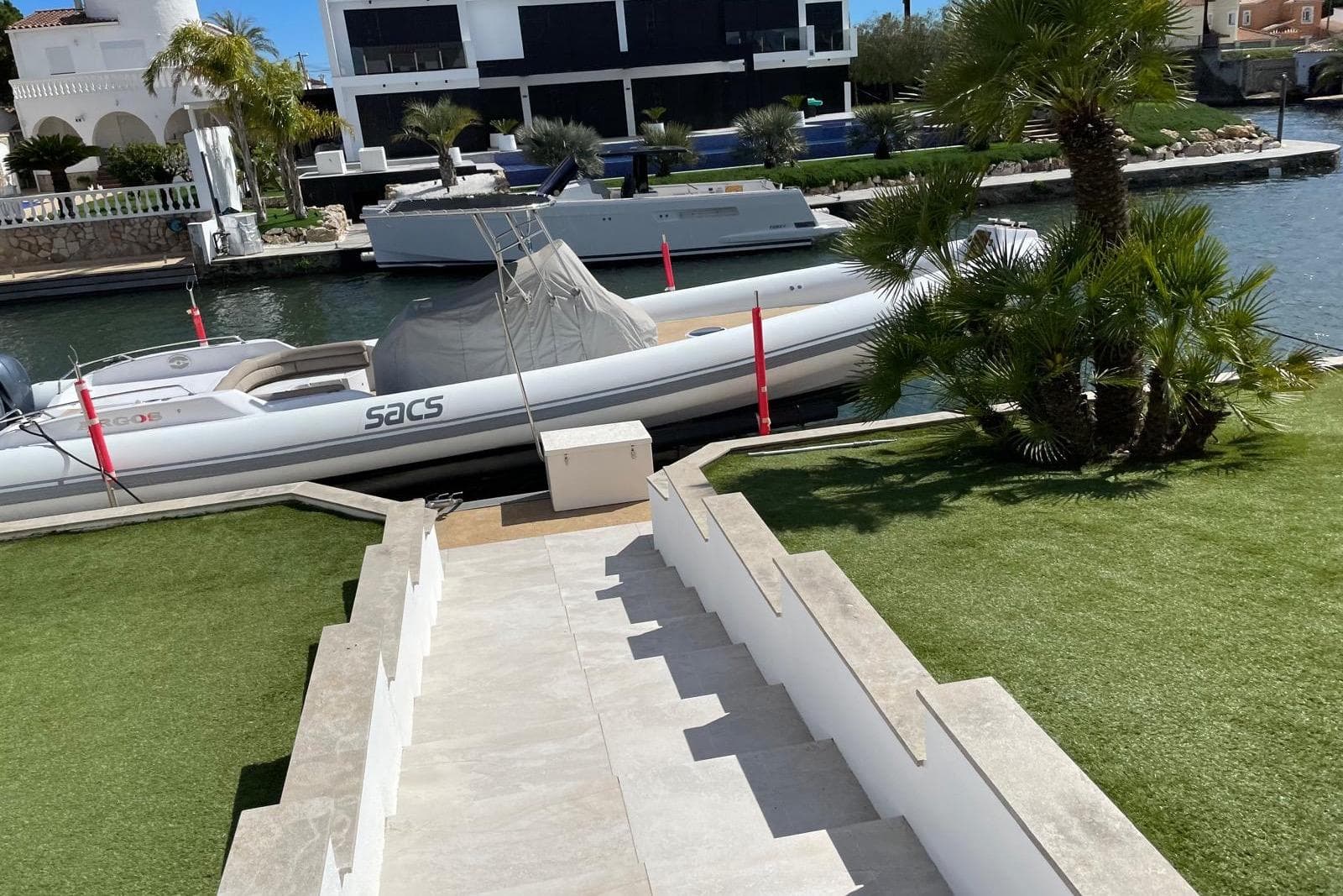 2010 SACS STRATOS boat docked by a canal, surrounded by lush greenery and modern architecture.