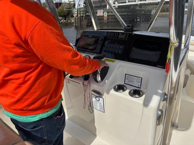 Person operating 2022 Scout 215 XSF boat's helm with modern controls.