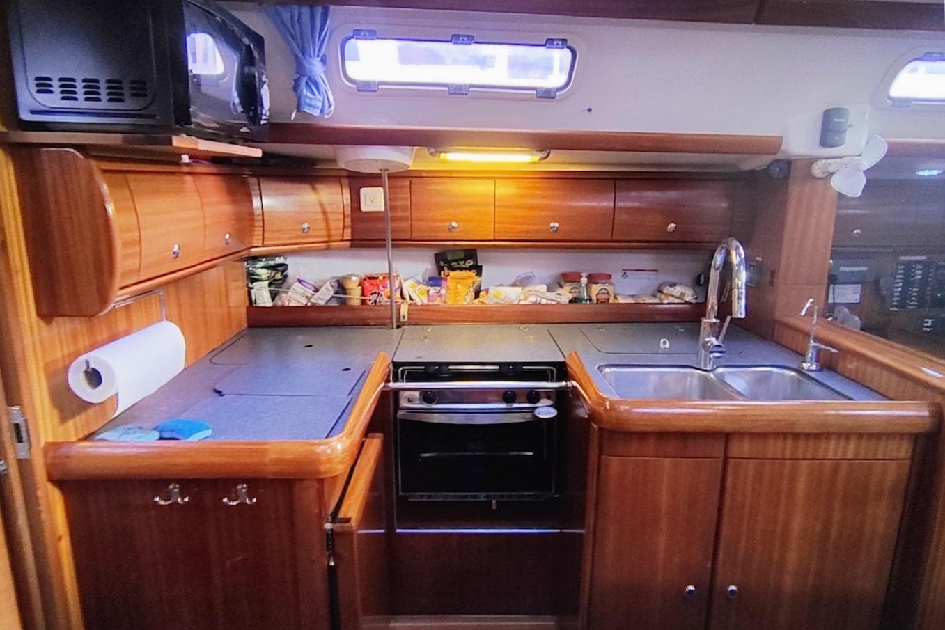 Galley kitchen in 2003 Bavaria 49 yacht with wooden cabinetry and modern appliances.