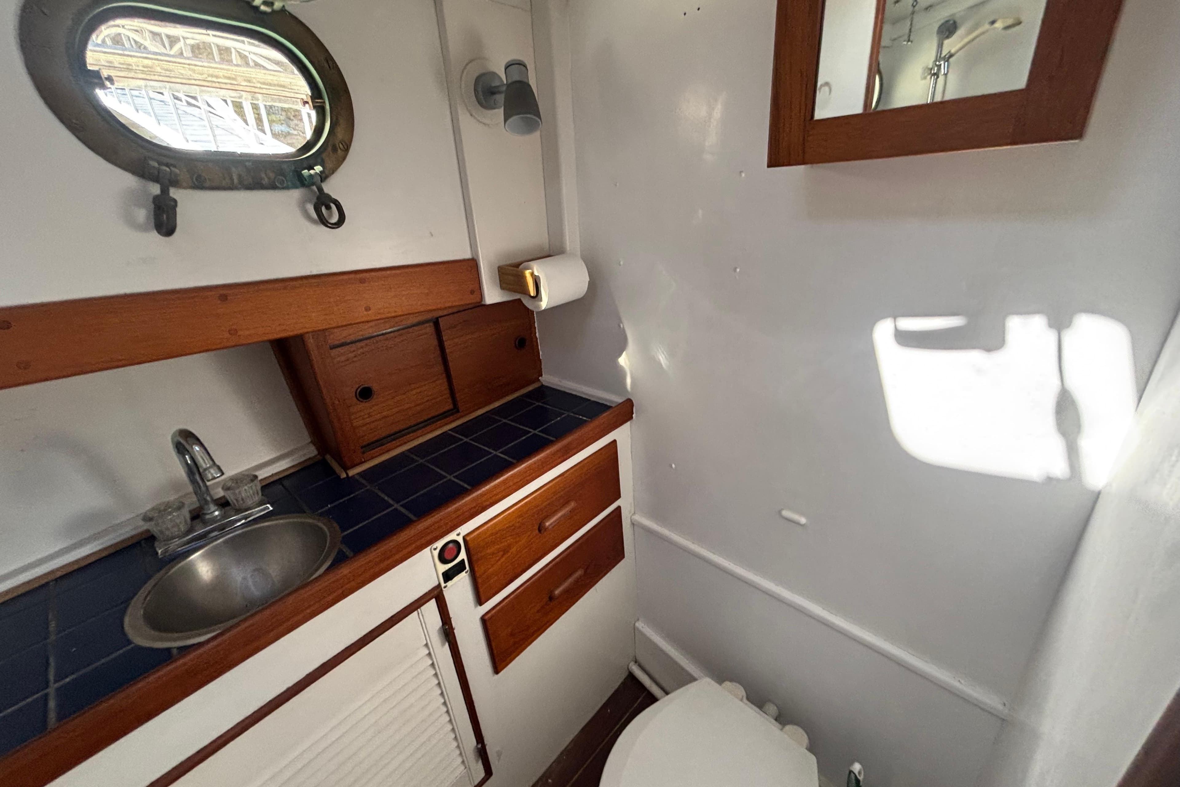Compact bathroom in a 1985 Jarvis Newman 36 boat with wooden accents and porthole window.