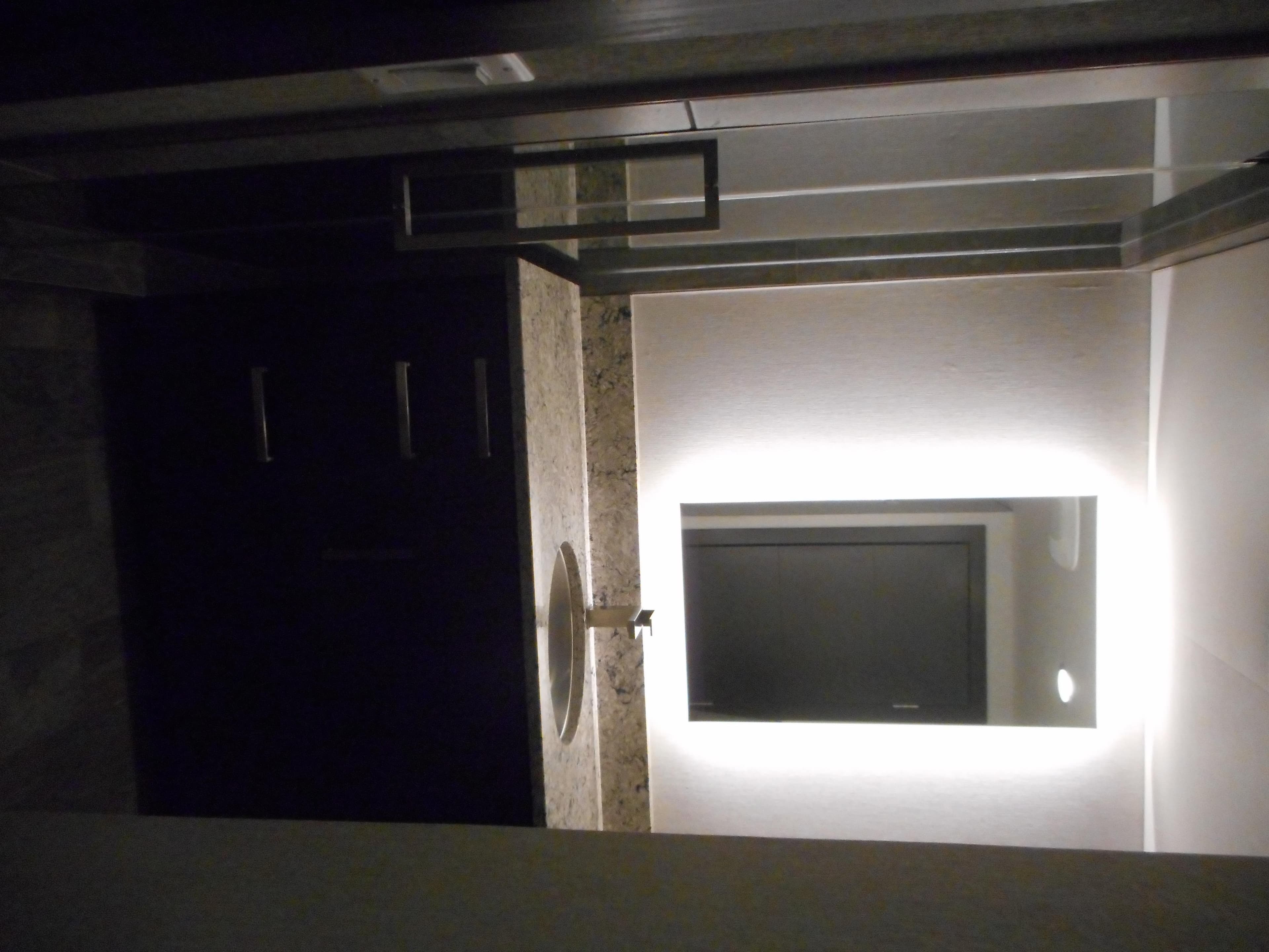 Modern bathroom with illuminated mirror and granite countertop, featuring Adonia Liquidity Trip 5 design.