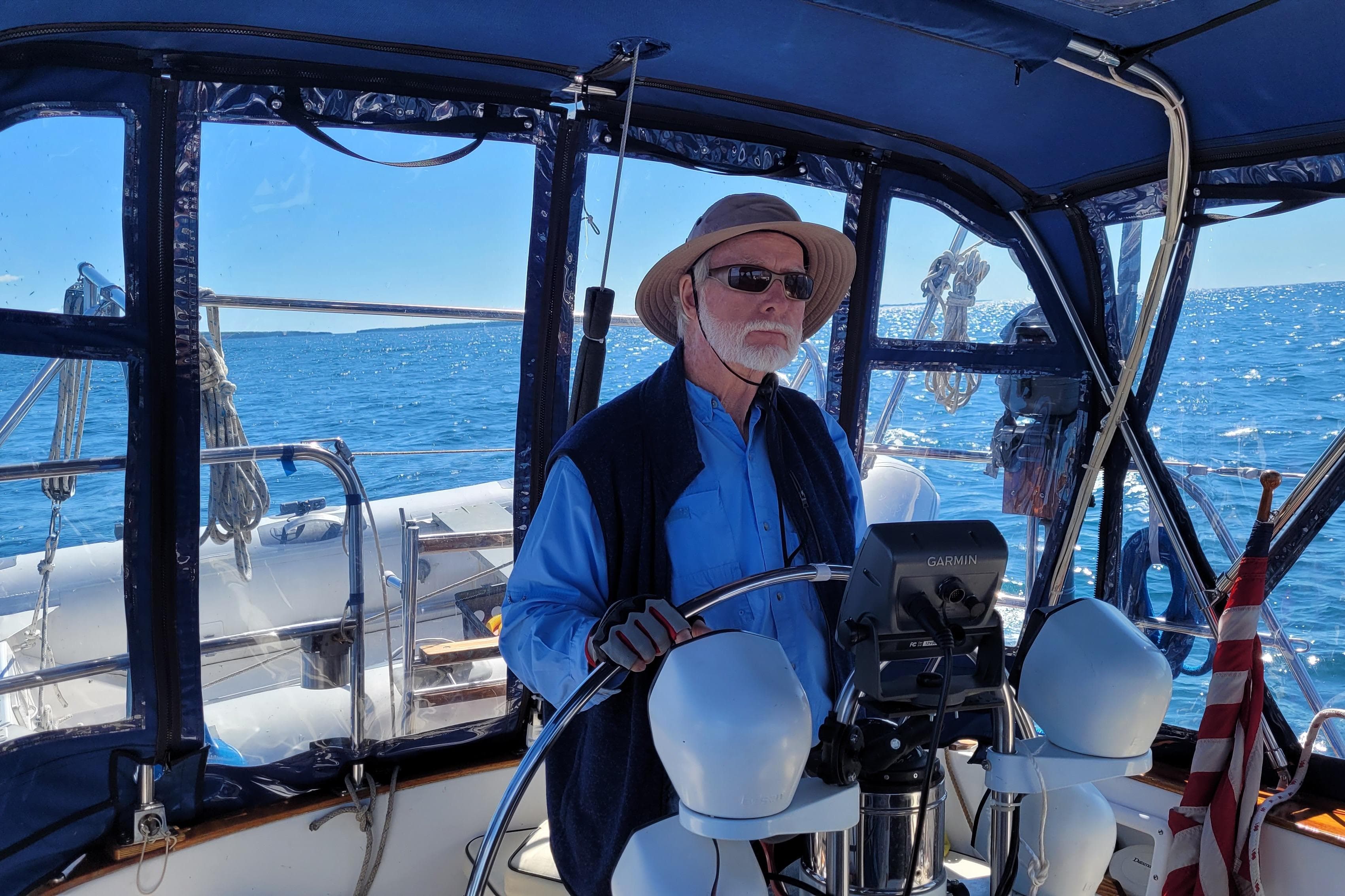 Man steering 1984 Endeavour 35 sailboat on open sea under clear blue sky.