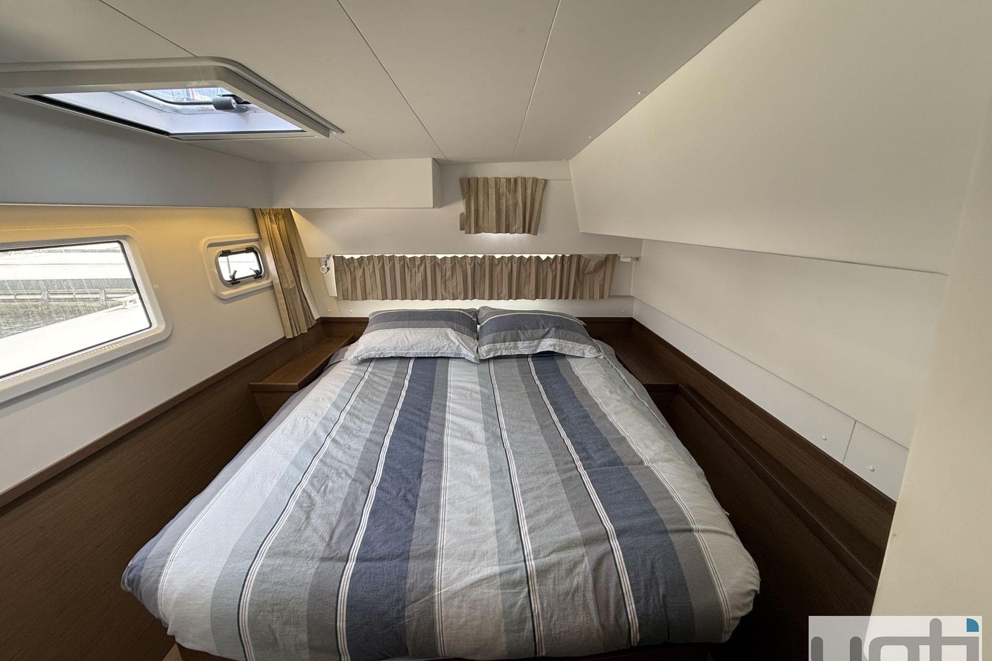 Cozy bedroom in 2019 Lagoon 42 catamaran with striped bedding and ample natural light.