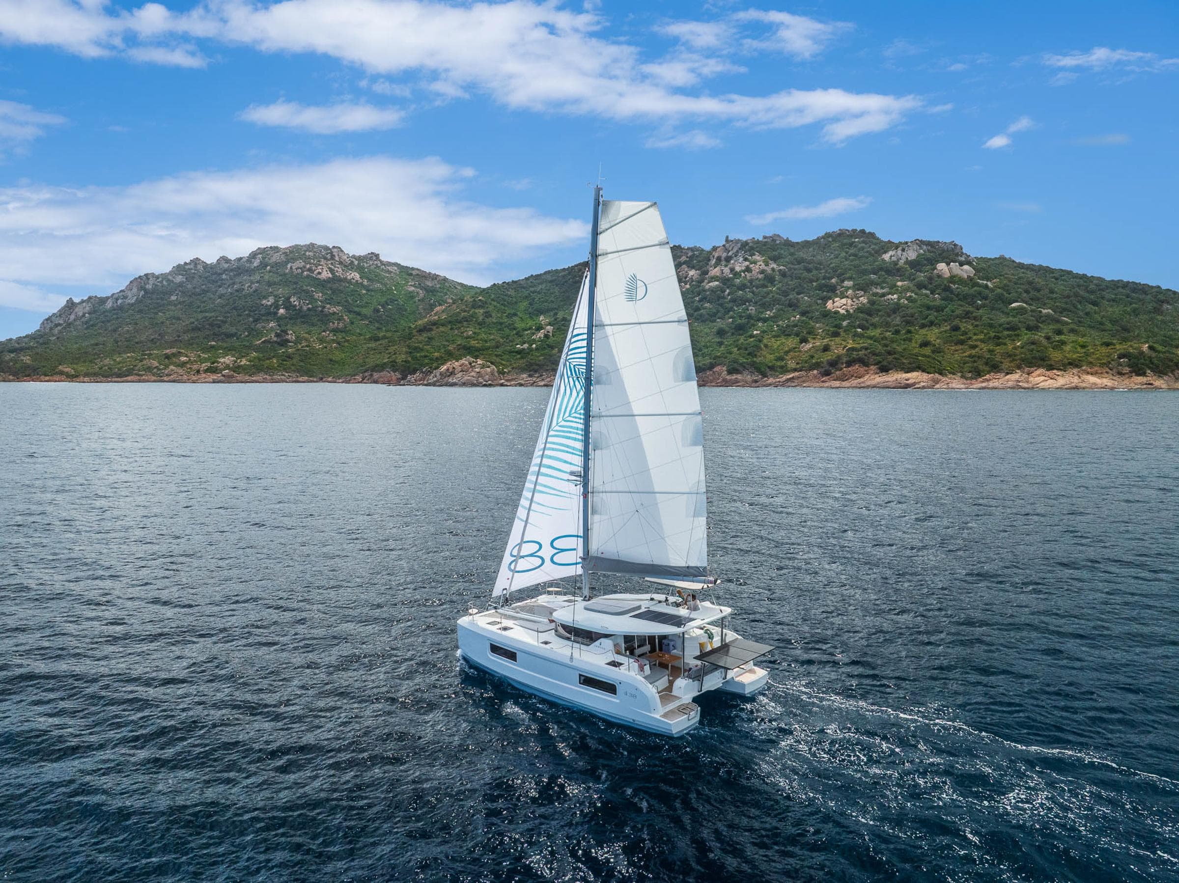 2025 Lagoon 38 catamaran sailing near a scenic coastline under a clear blue sky.