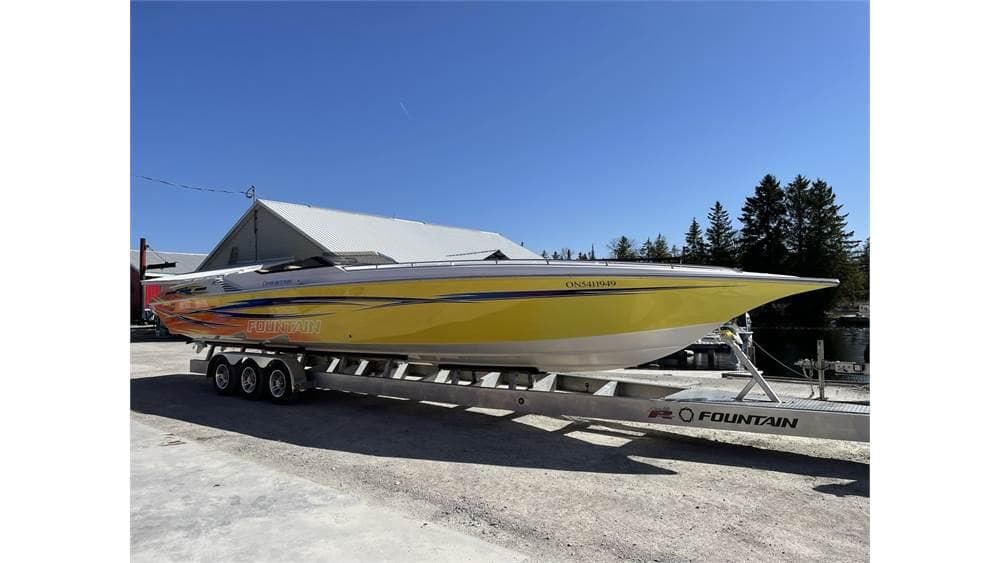 Yellow 2006 Fountain 42 speedboat on trailer, parked outdoors under clear blue sky.