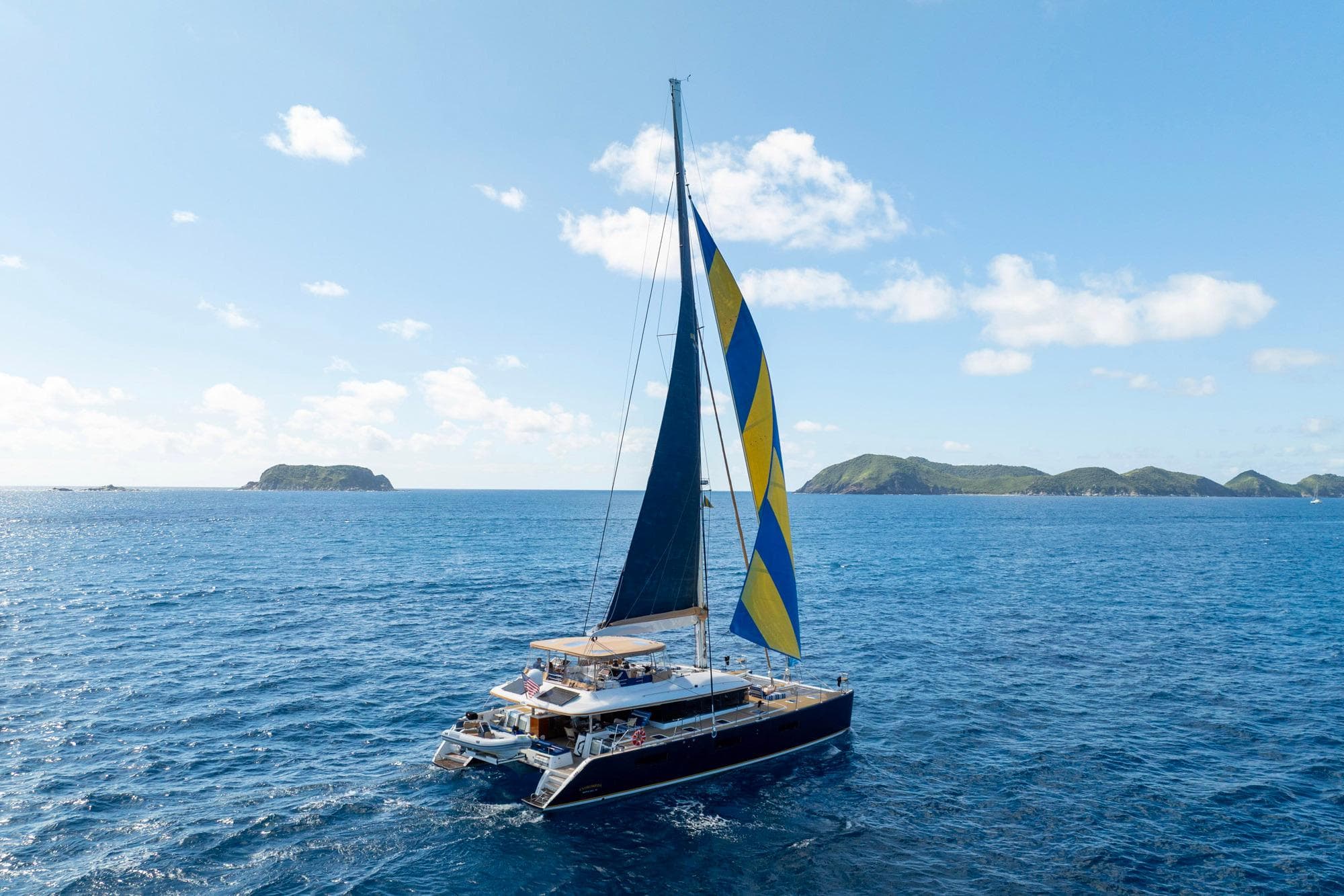 Sailing Lagoon 620 catamaran, 2016 model, cruising in clear blue ocean with distant islands.