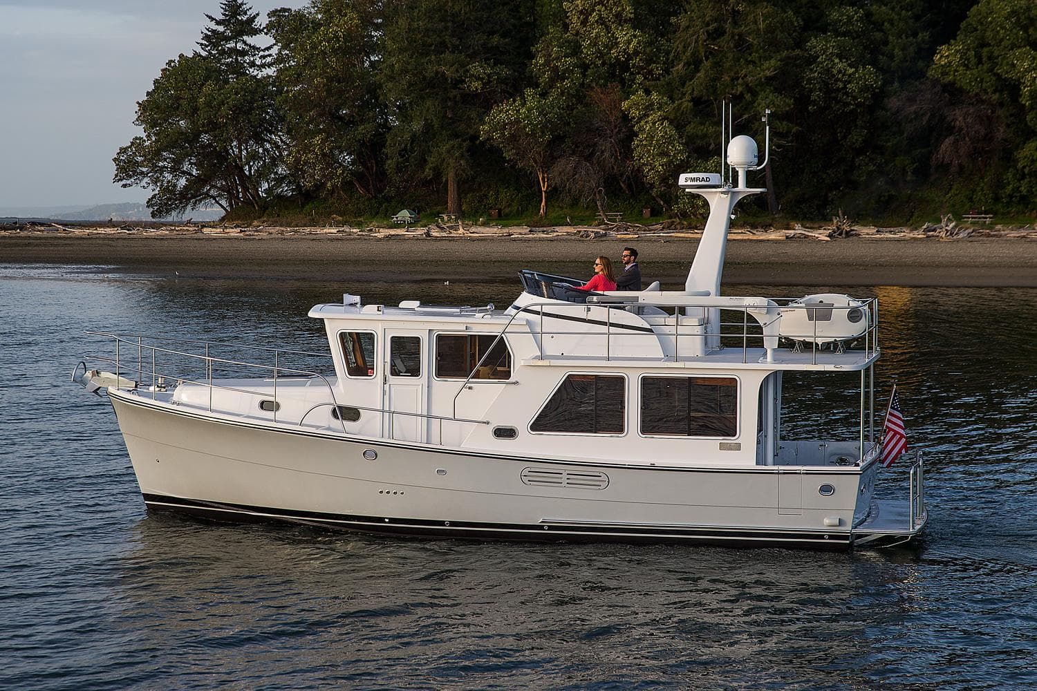 2025 Helmsman Trawlers 38E Pilothouse cruising near a forested shoreline.