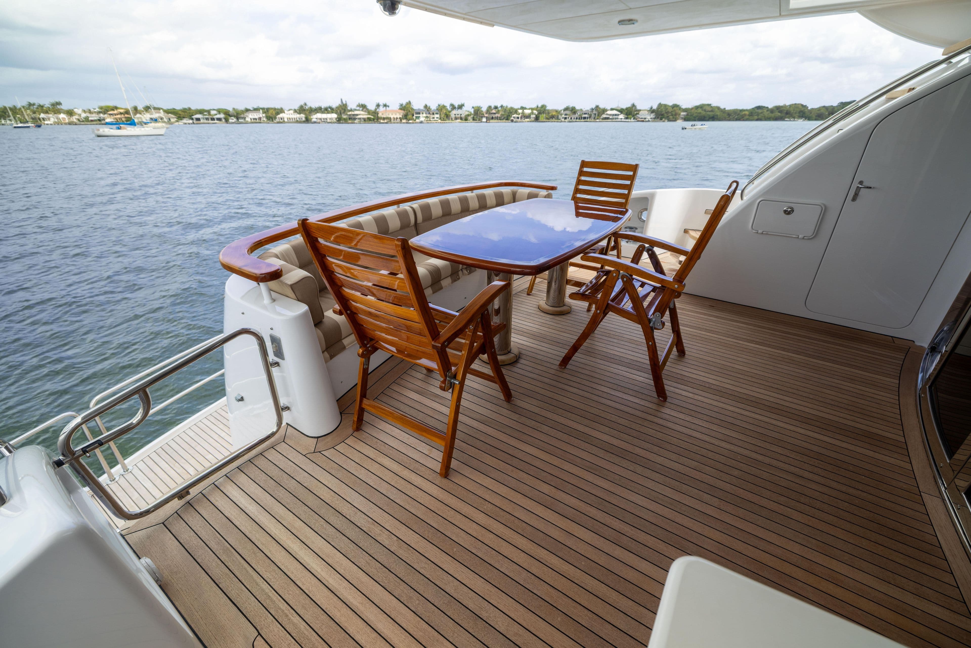Outdoor deck of 2005 Hatteras 80 Motor Yacht with wooden furniture and ocean view.