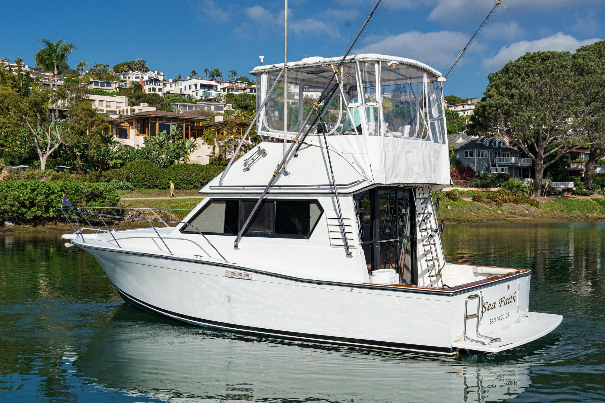 1989 Pearson 34 Convertible yacht on calm water, surrounded by lush greenery and coastal homes.