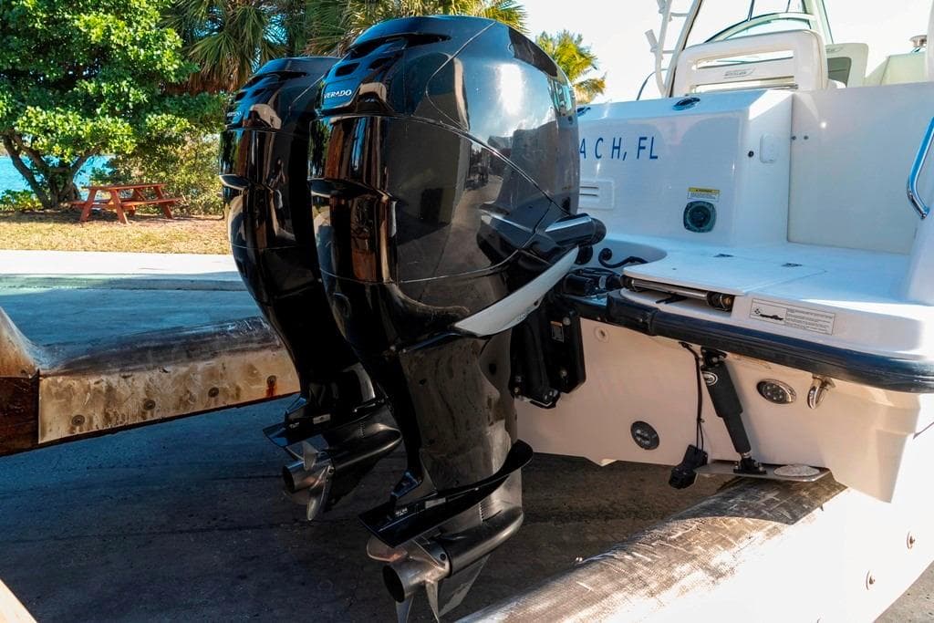 2014 Boston Whaler 315 Conquest with dual outboard engines, docked near a scenic beach.