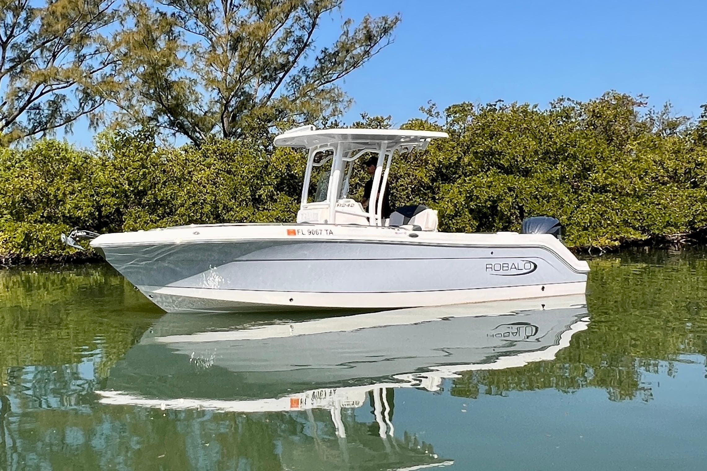 2021 Robalo R242 Explorer boat on calm water, surrounded by lush greenery.