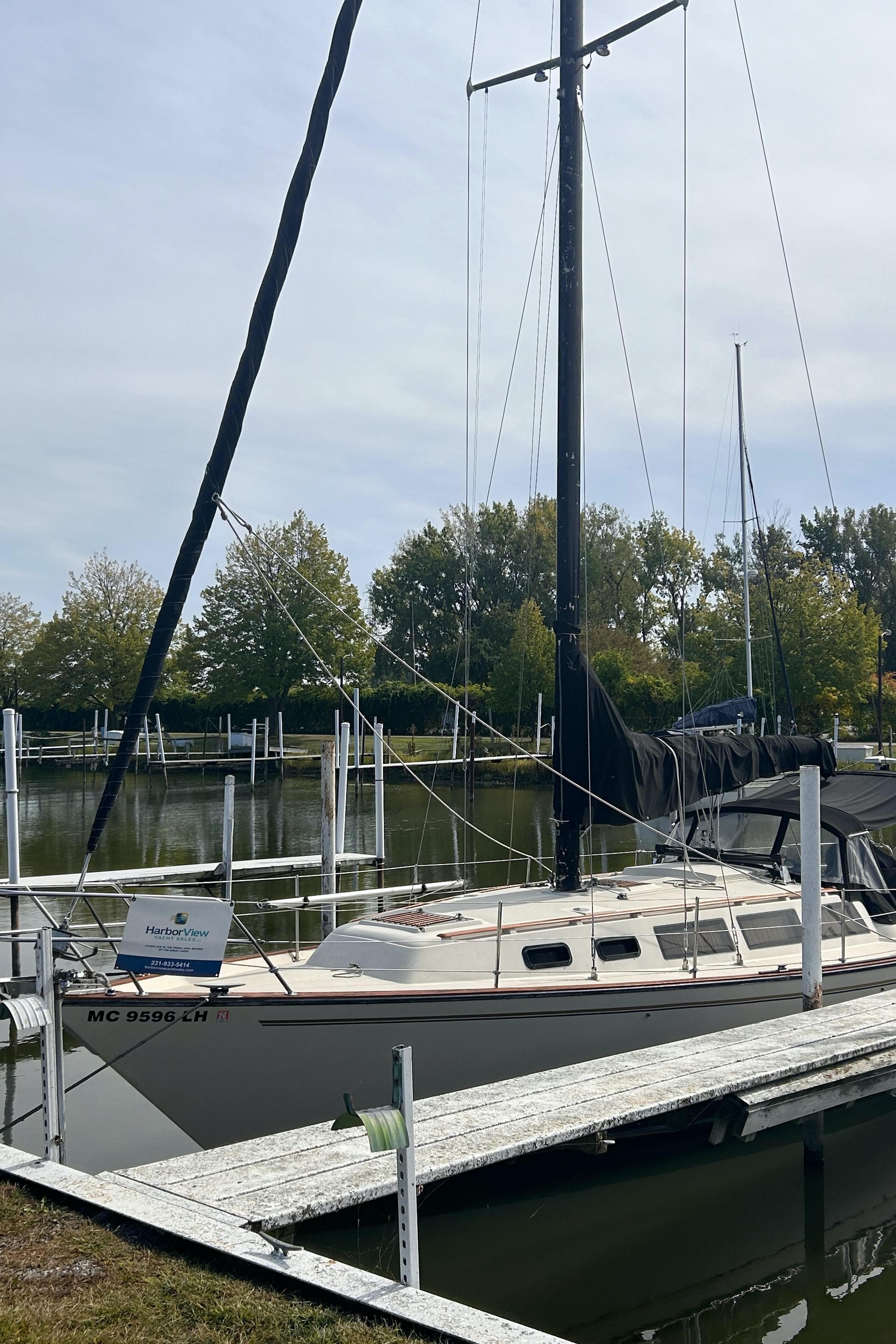 1982 S2 11.0 A sailboat docked at a marina with trees in the background.