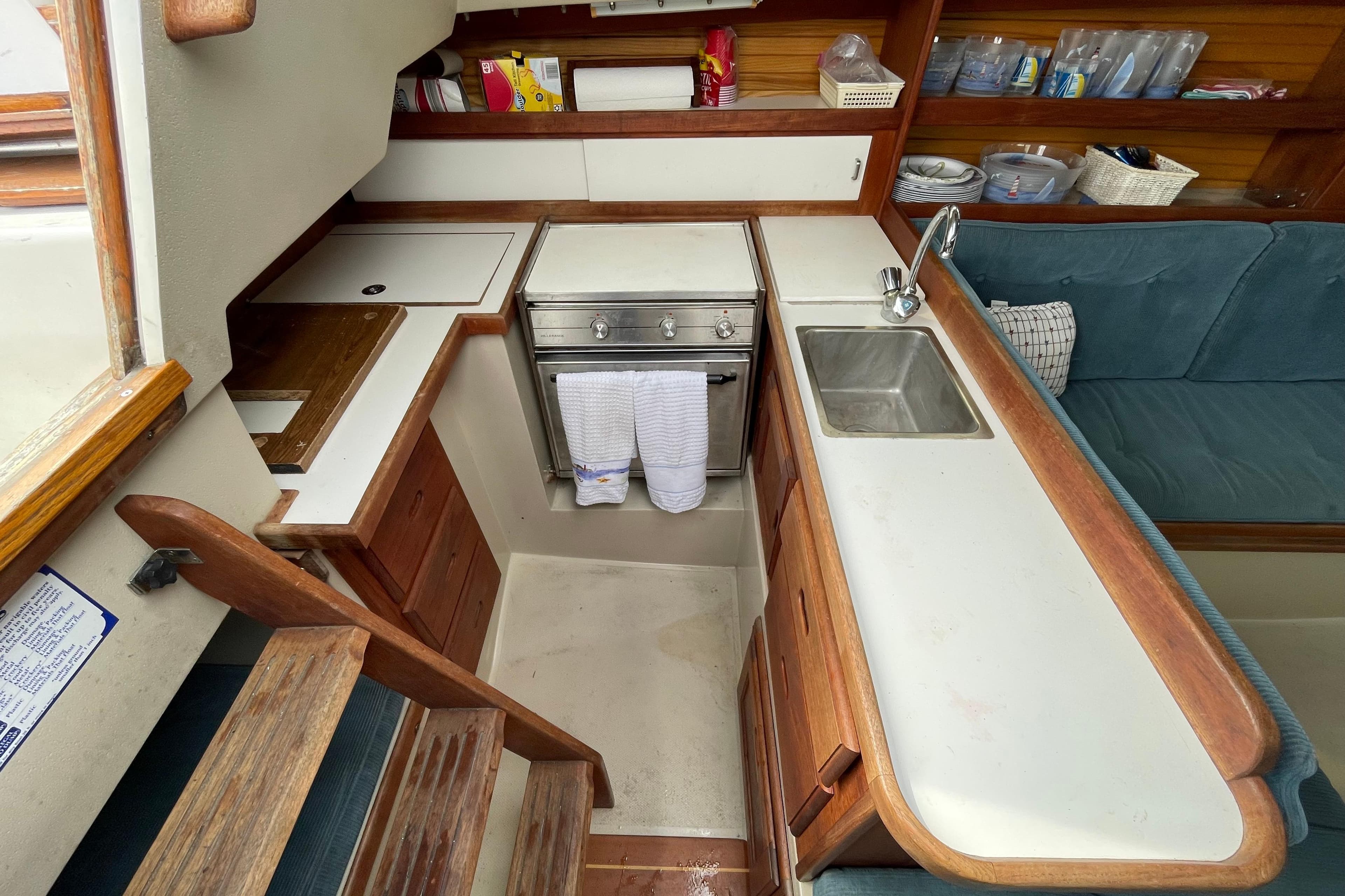 Interior of 1989 Catalina 30 sailboat kitchen with stove, sink, and wooden cabinetry.