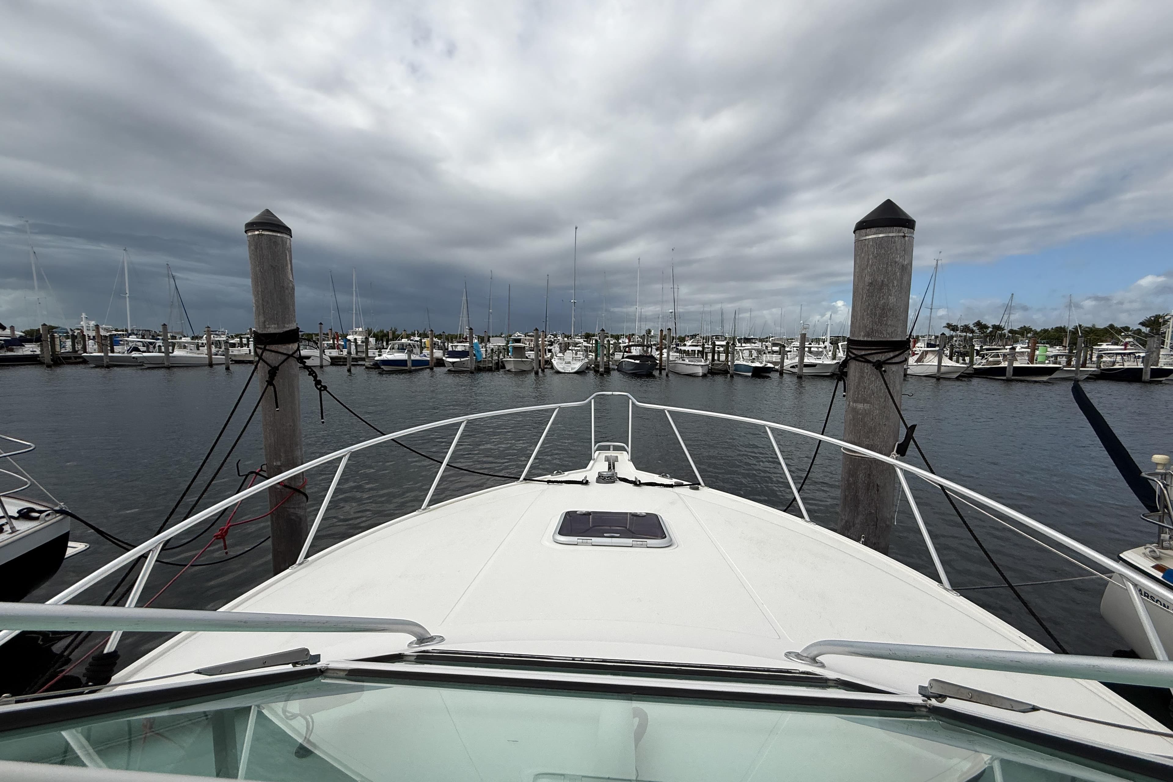 Bow view of 1998 Cabo 31 Express yacht docked in a marina under cloudy skies.