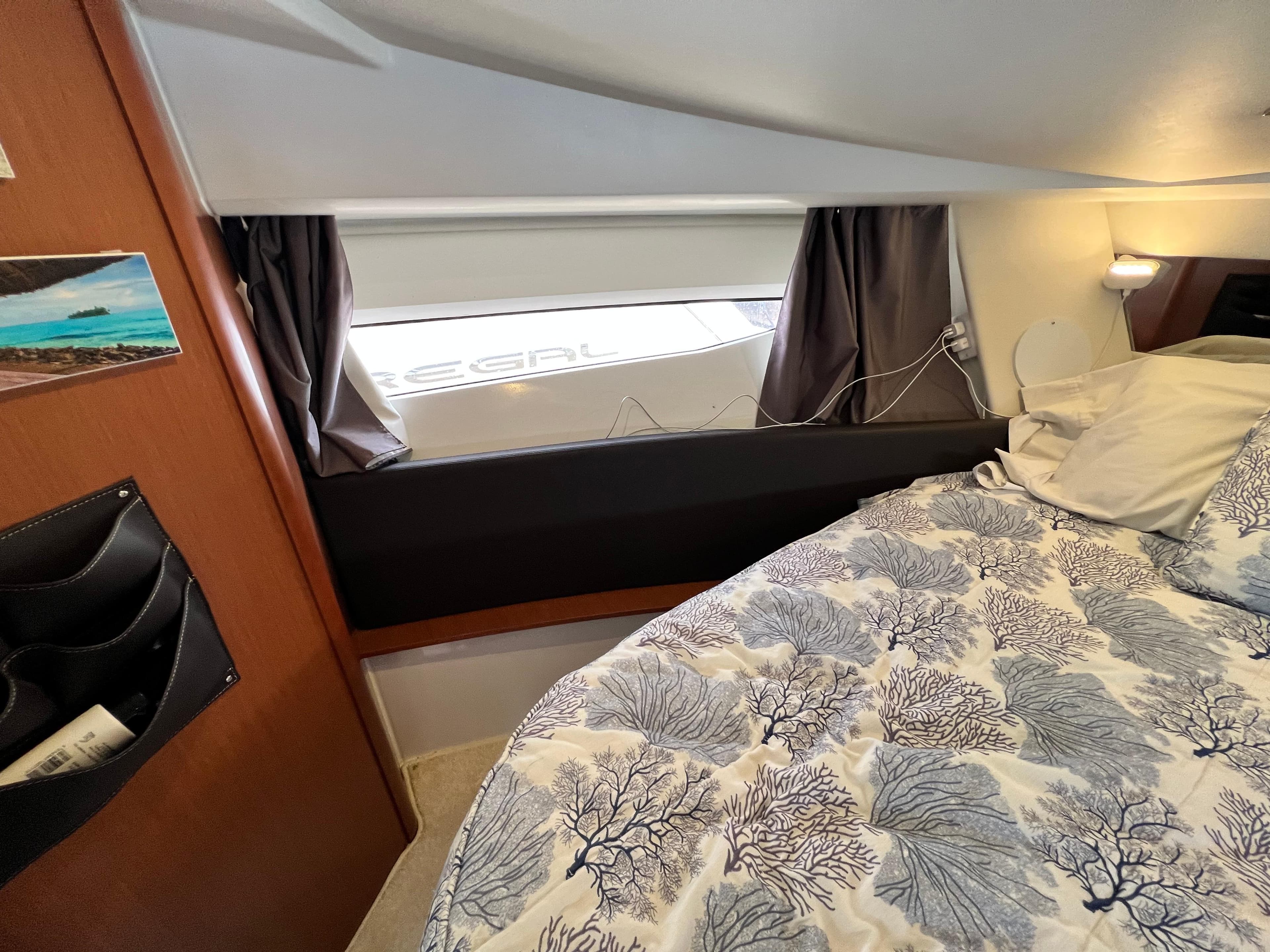 Cozy cabin interior of 2017 Jeanneau NC11 with patterned bedding and window view.