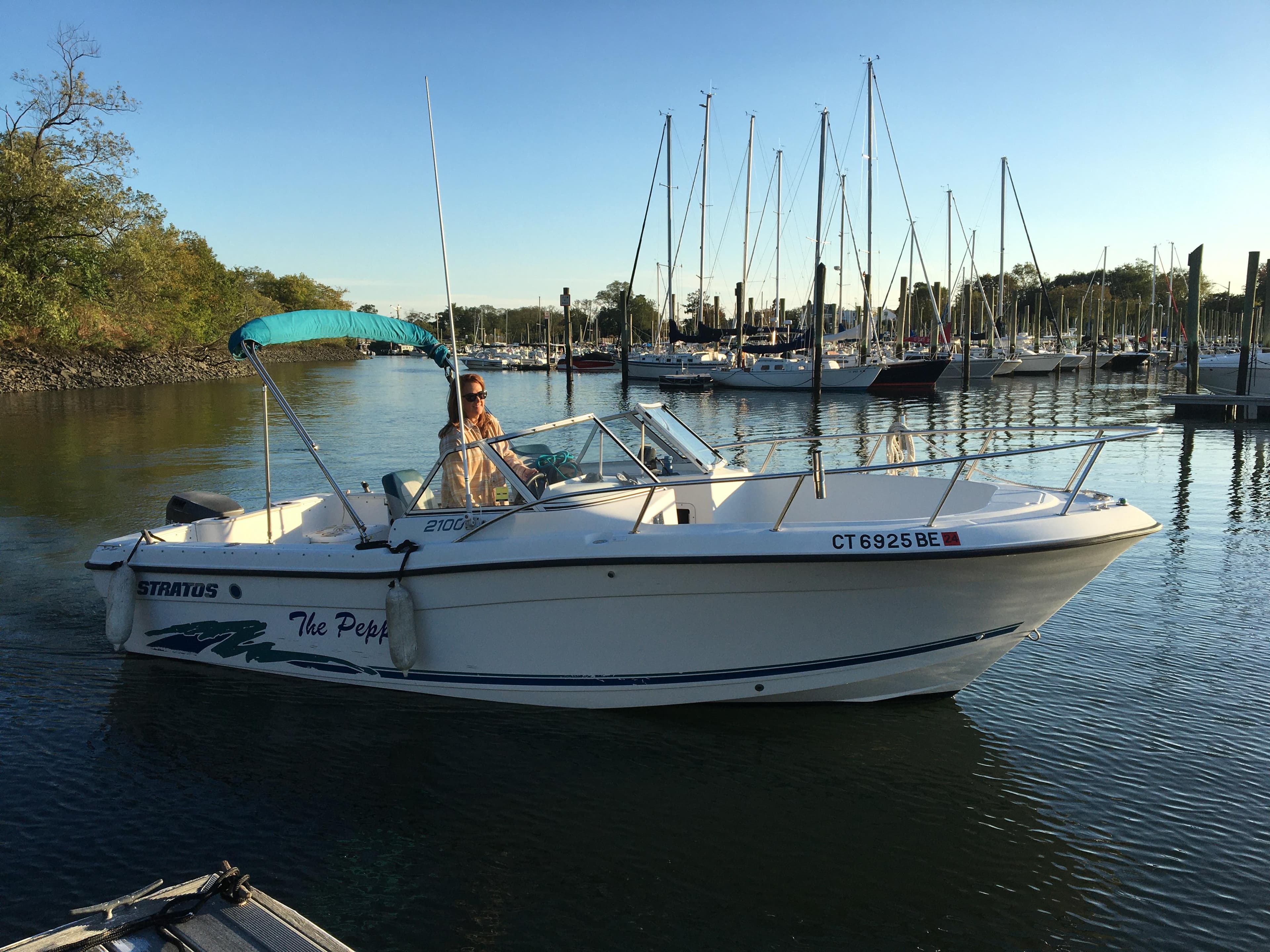 1998 Stratos 2100 boat cruising in a marina with sailboats in the background.