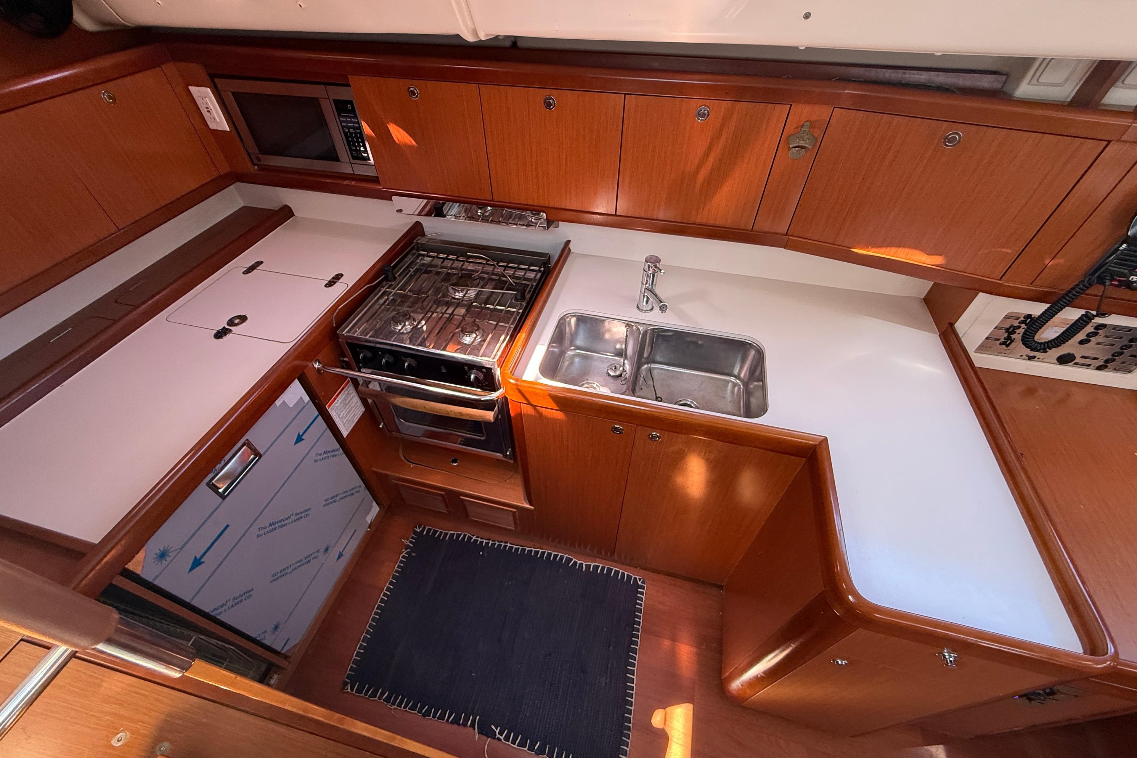 Interior of 2010 Beneteau Oceanis 43 yacht kitchen with stove, sink, and wooden cabinetry.