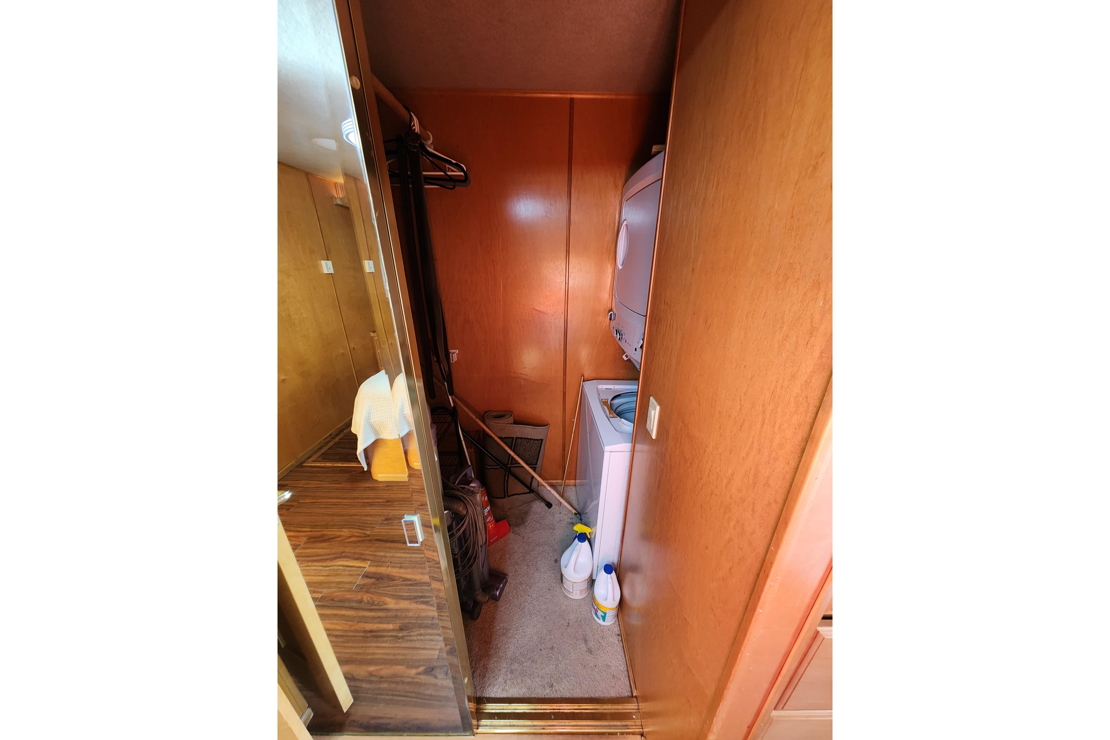 Laundry room with stacked washer-dryer, cleaning supplies, and wooden walls in Sharpe 85, 2000 model.