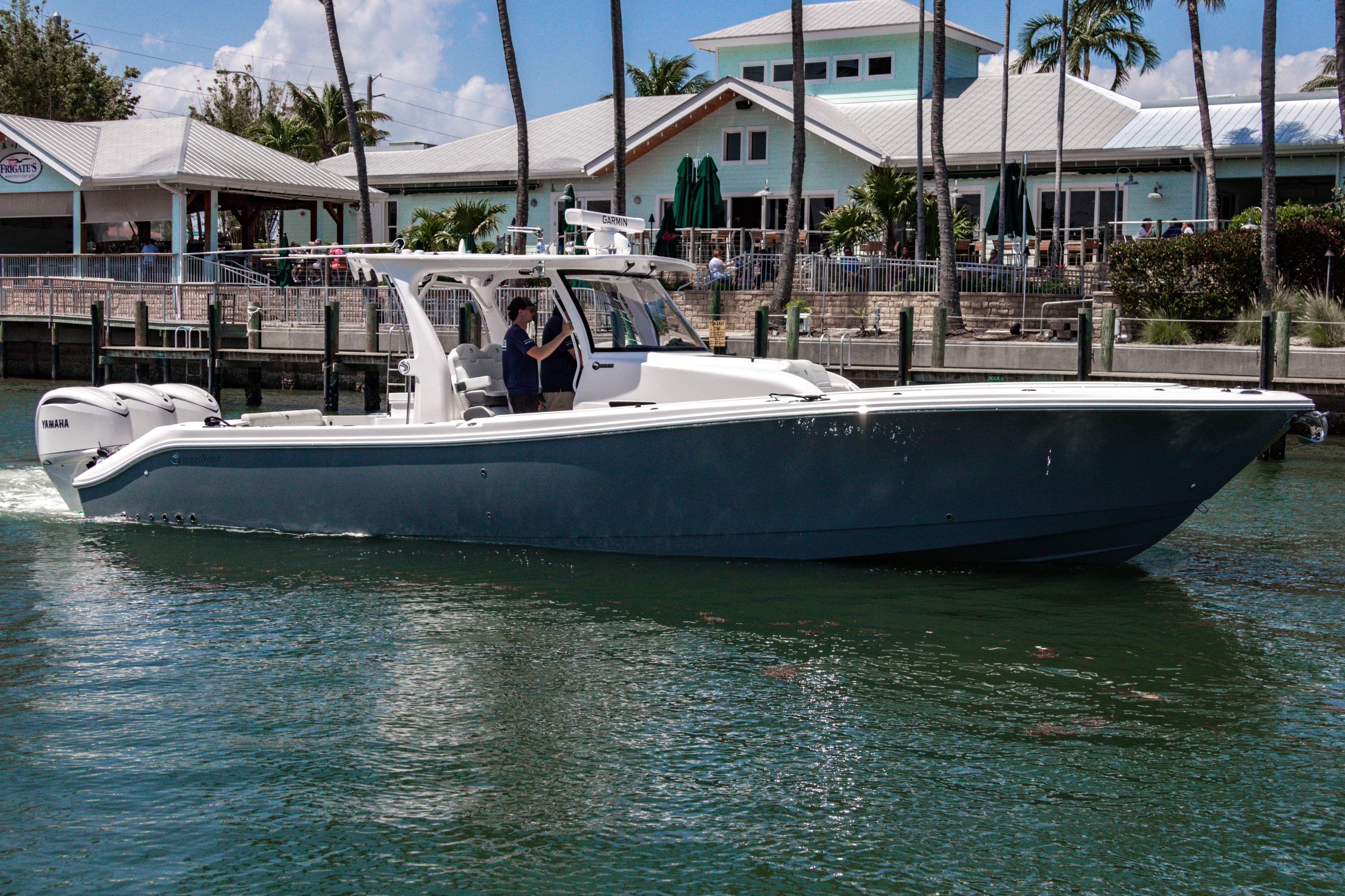 2025 Edgewater 370CC boat cruising near waterfront buildings and palm trees.
