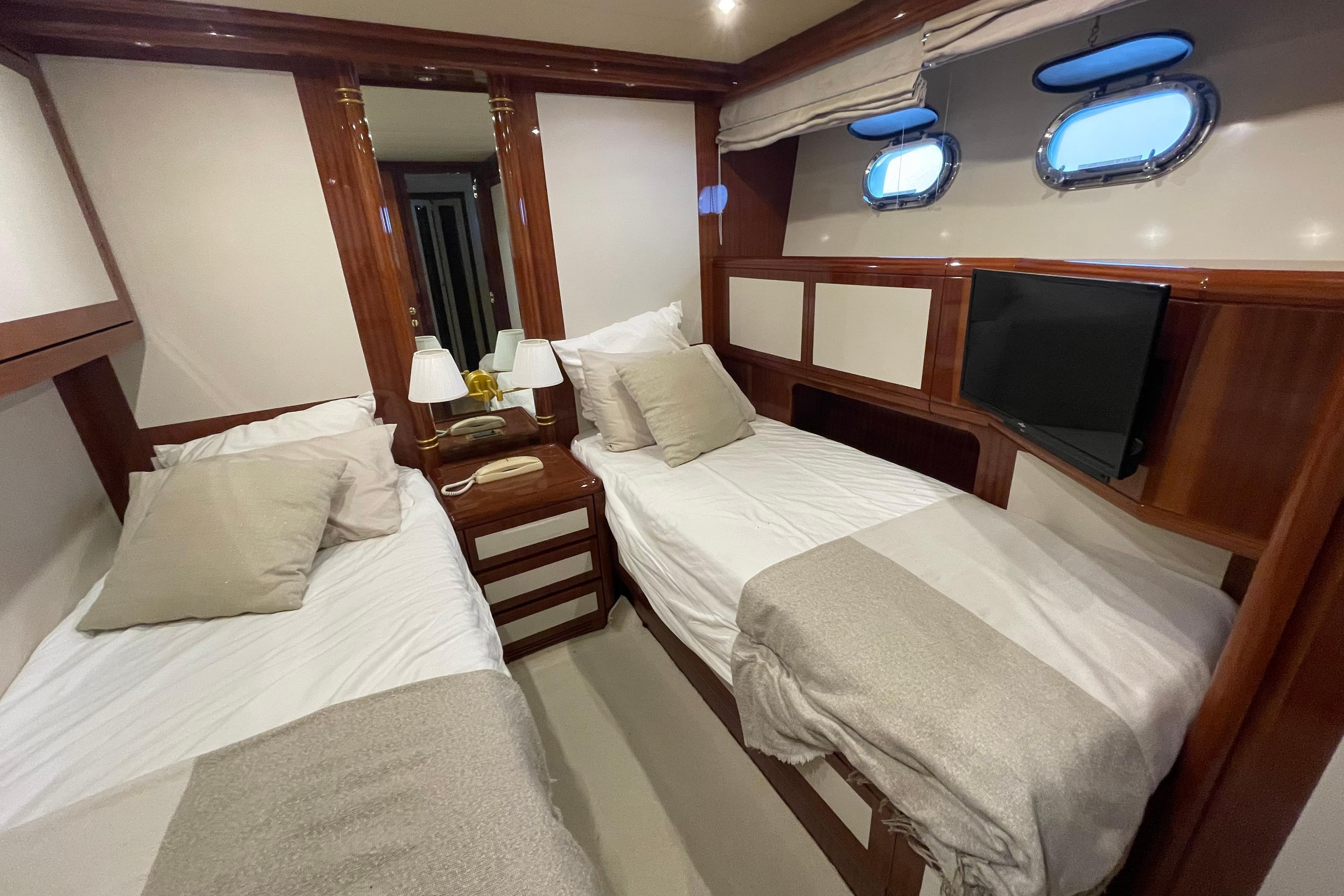 Luxurious 1999 Mangusta 72 yacht cabin with twin beds, elegant wood finish, and porthole windows.