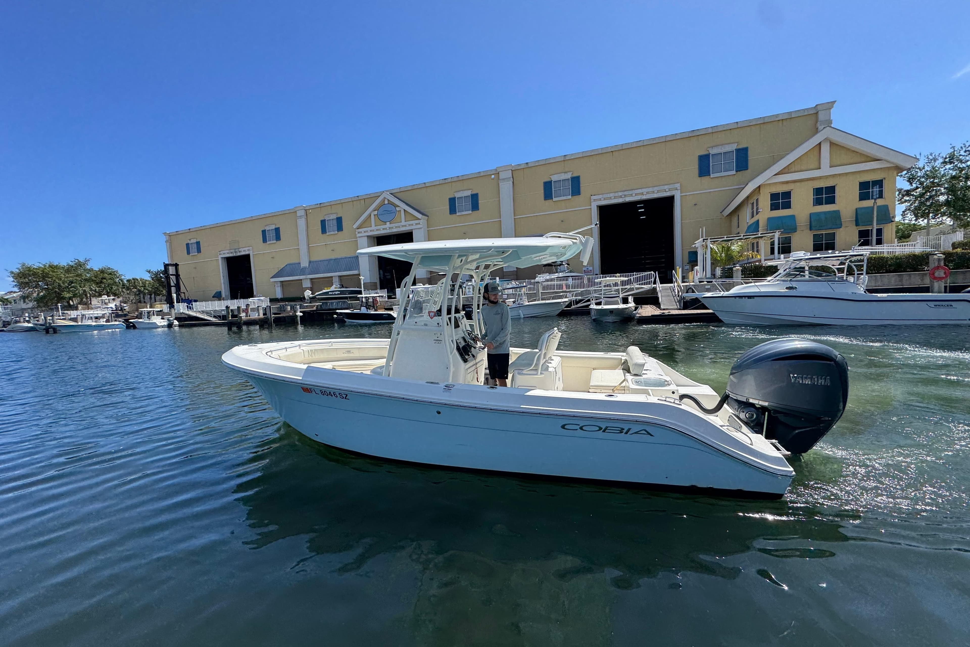 2021 Cobia 237 Center Console boat docked near a marina building.