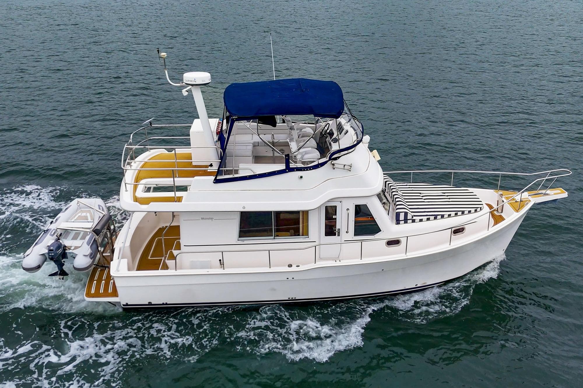 2011 Mainship 395 Trawler cruising on open water with a small dinghy attached.