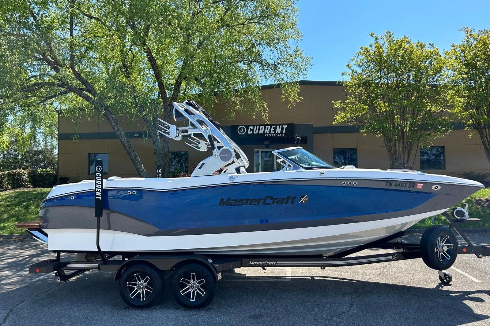 2021 MasterCraft X24 boat on trailer, parked outdoors near trees and building.