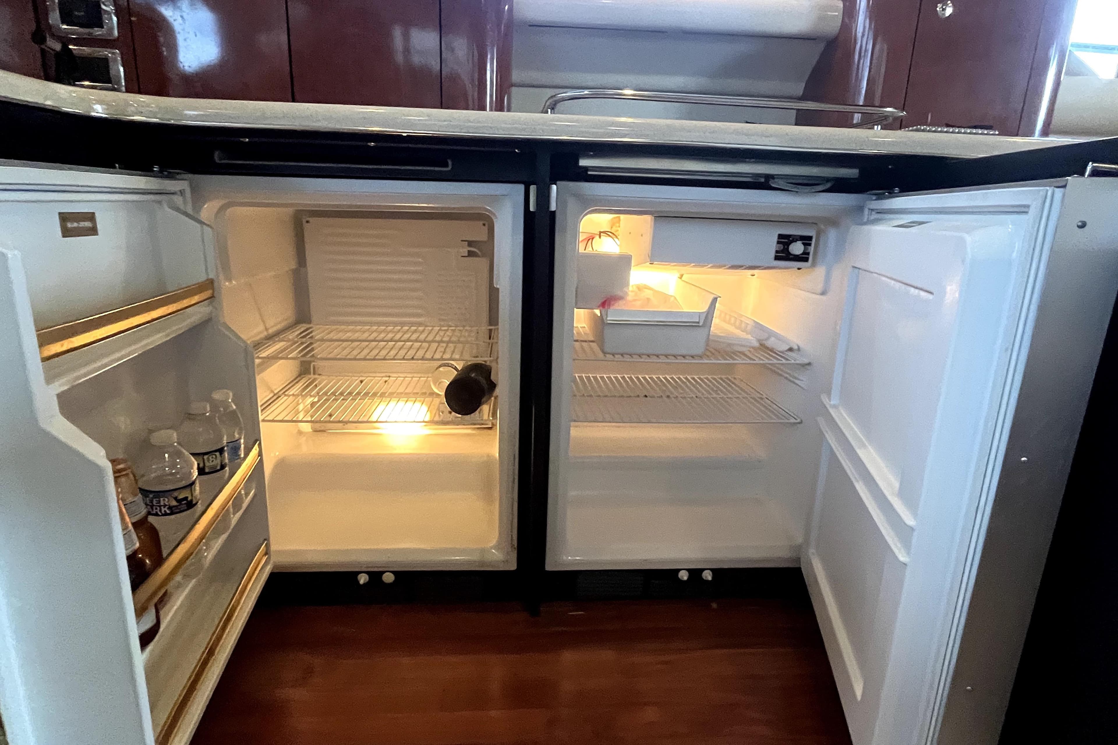 Open refrigerator inside 2003 Sea Ray 480 Sedan Bridge yacht, displaying beverages and empty shelves.
