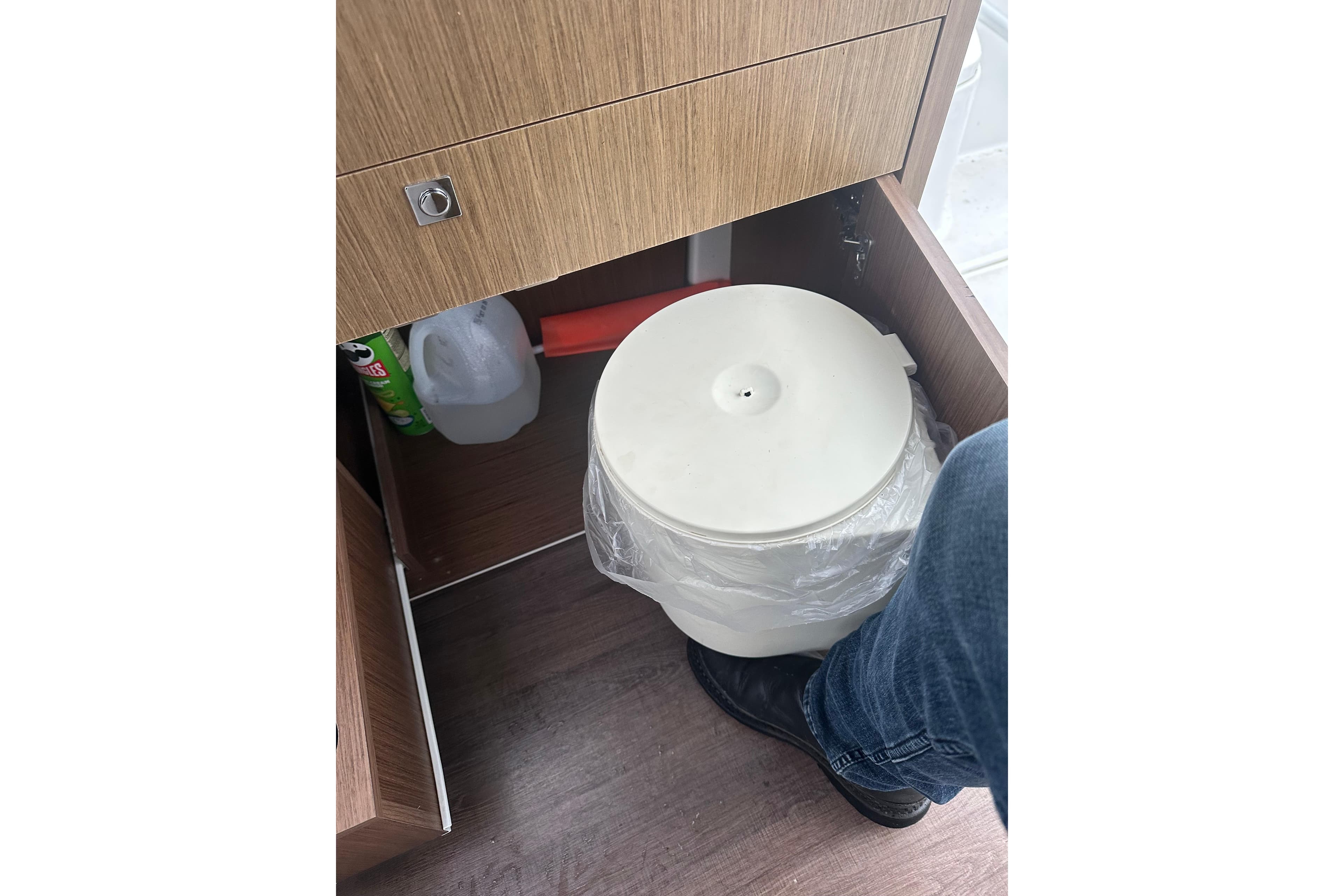 Storage compartment in 2023 Beneteau Antares 9 with cleaning supplies and trash bin.