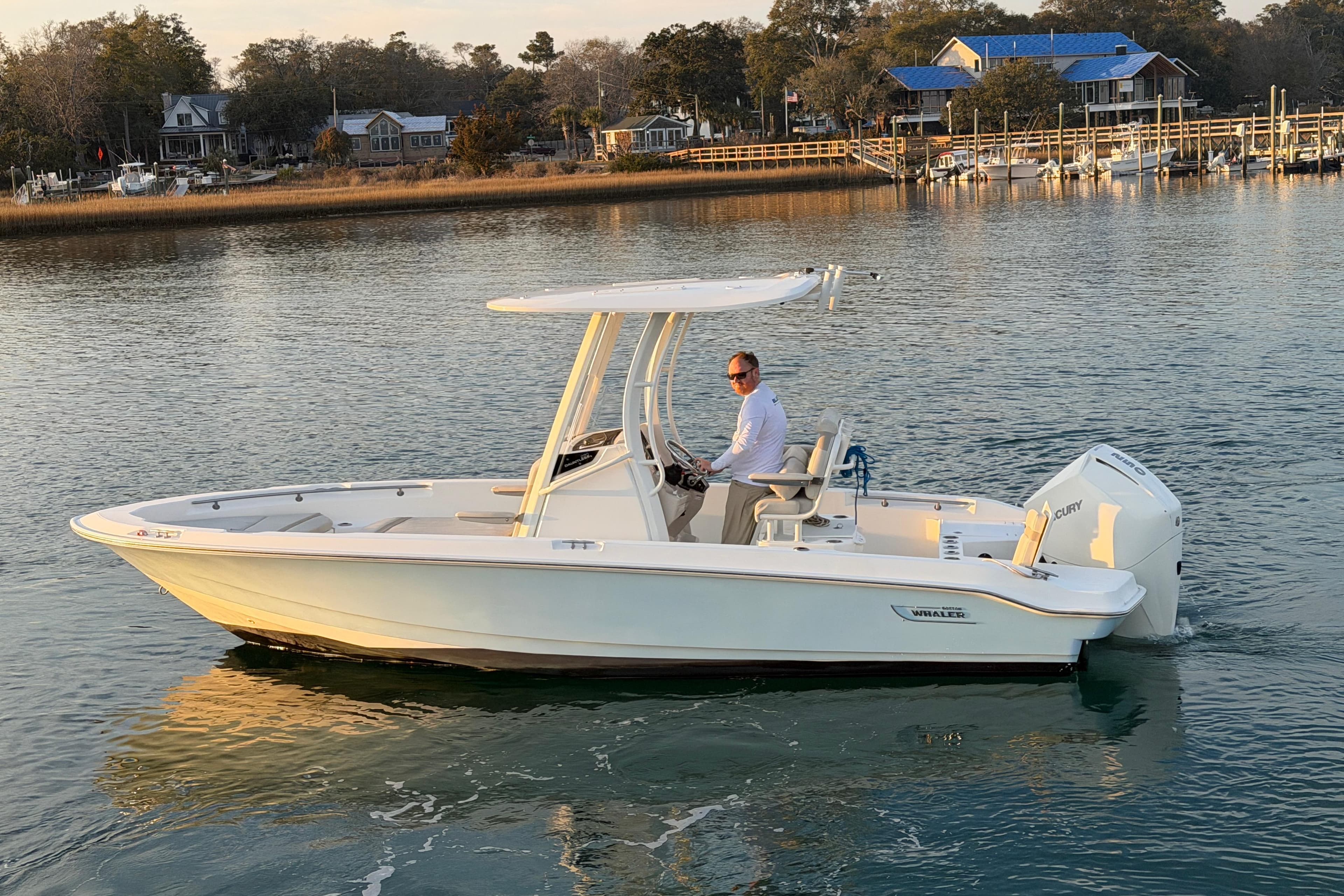 2023 Boston Whaler 220 Dauntless boat cruising on calm water near a dock.