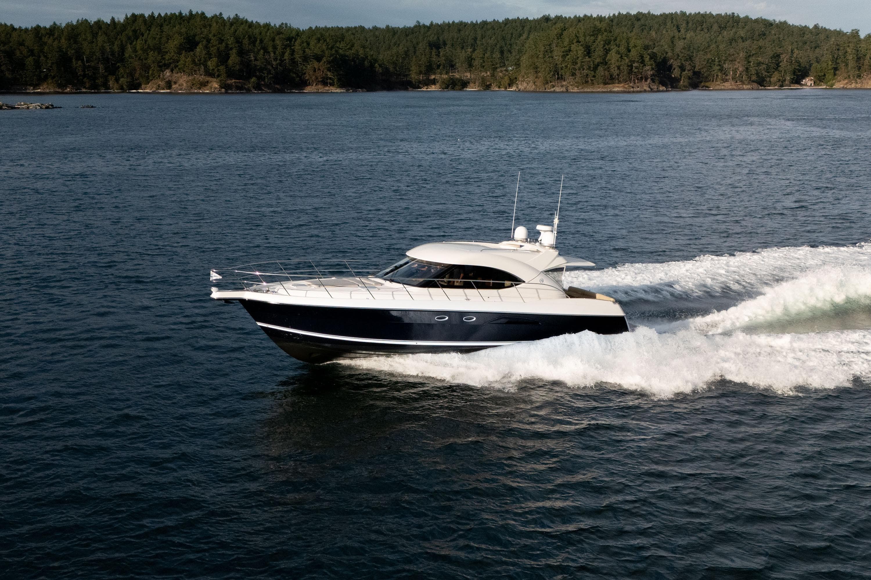 2011 Riviera 5000 Sport Yacht cruising on open water, surrounded by lush forested shoreline.