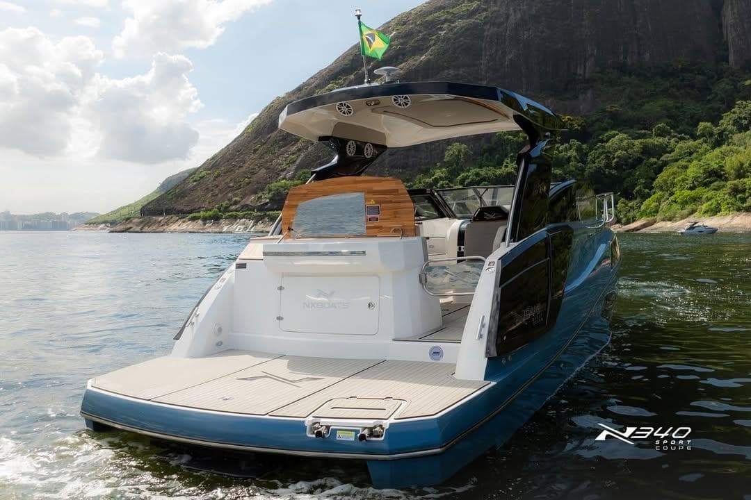 2026 NX Boats NX340 cruising near scenic coastline with lush greenery and rocky cliffs.