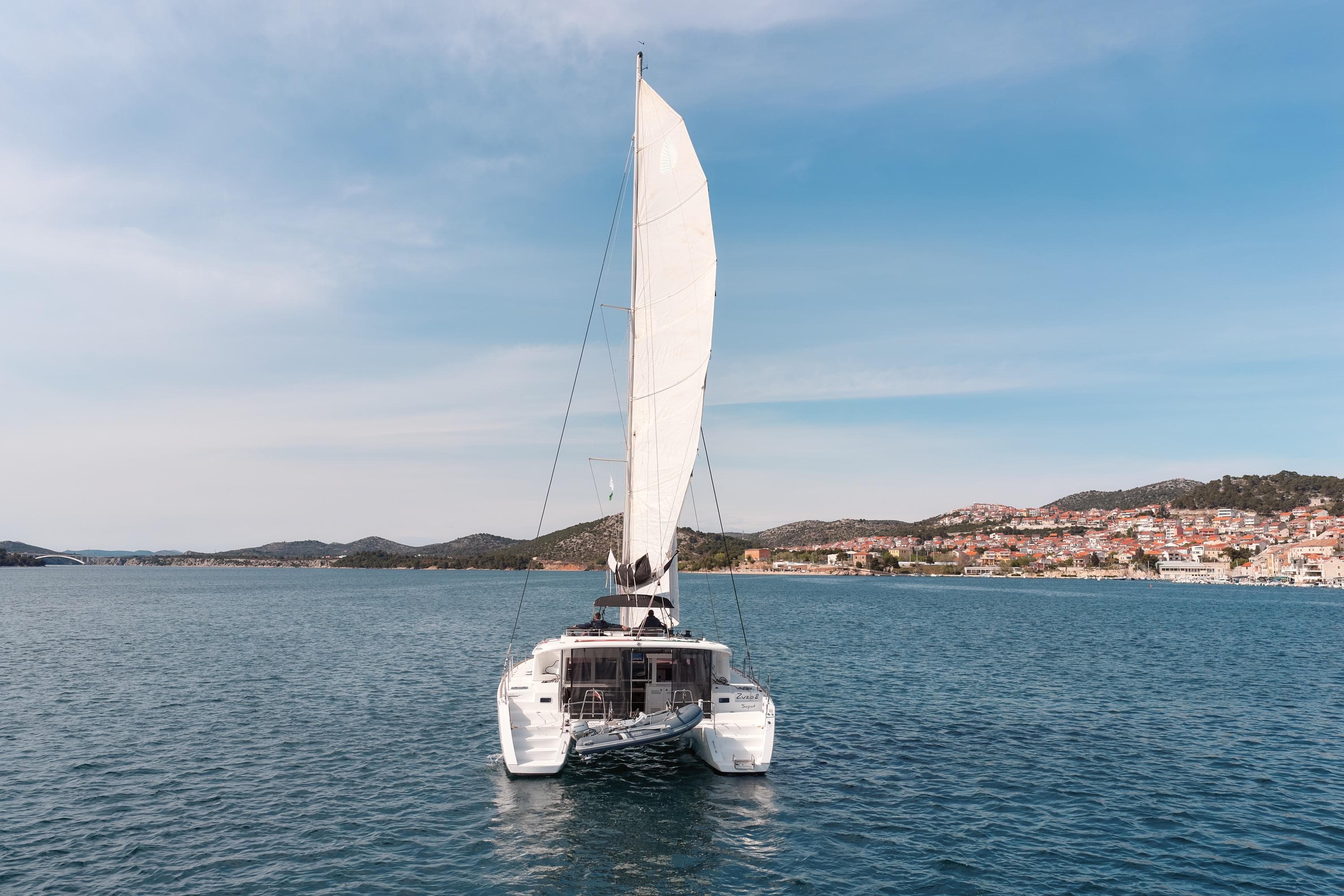 2018 Lagoon 450 catamaran sailing on calm waters near coastal town.