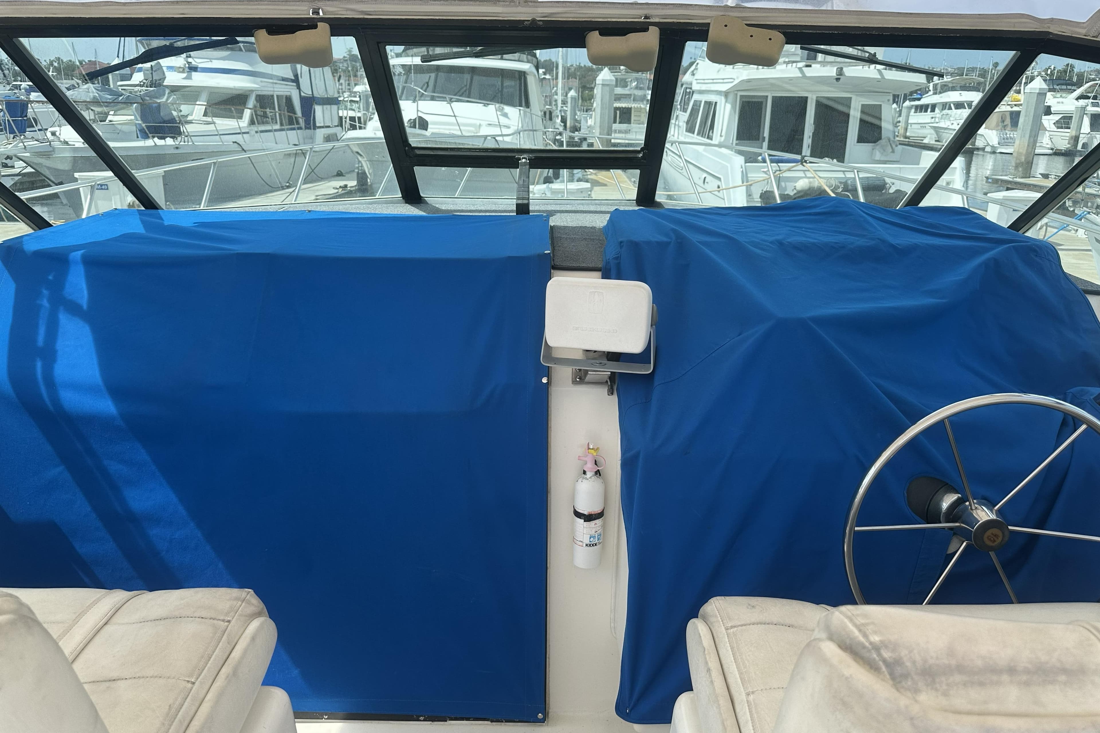 1990 Tiara Yachts 3600 Open cockpit with blue covers and steering wheel at marina.