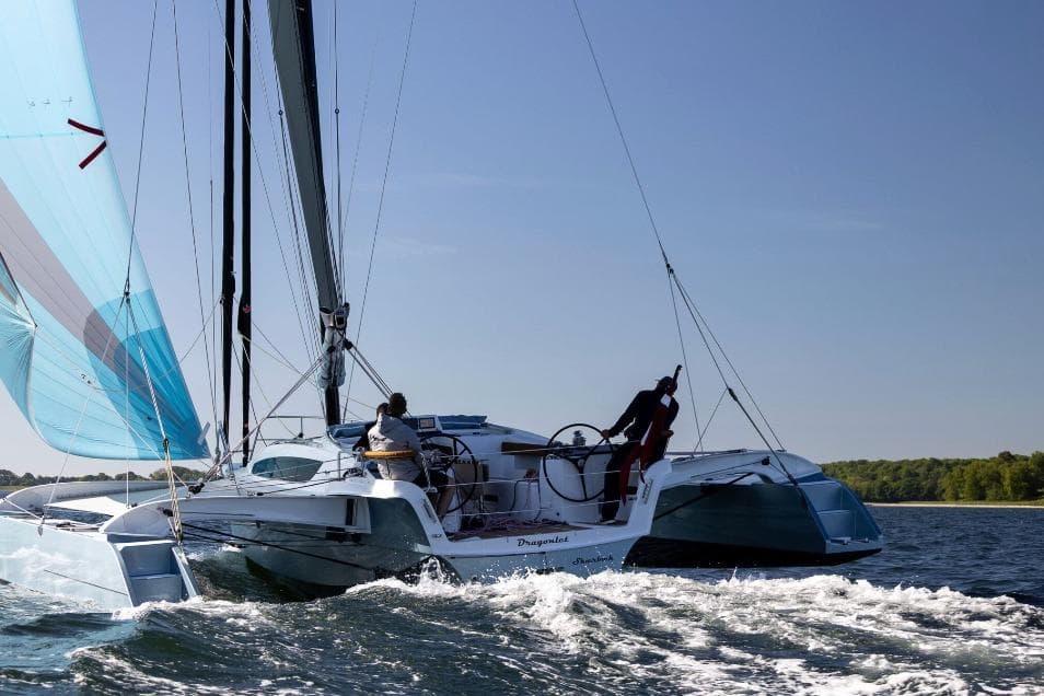 Sailing on a Dragonfly 36 trimaran, 2026 model, in open waters under clear skies.