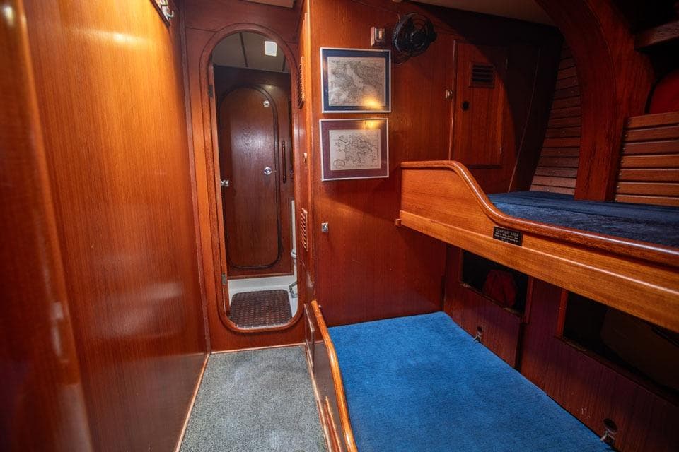 Interior of 1983 Nautor Swan 65 yacht with wooden paneling and blue carpeted bunk beds.