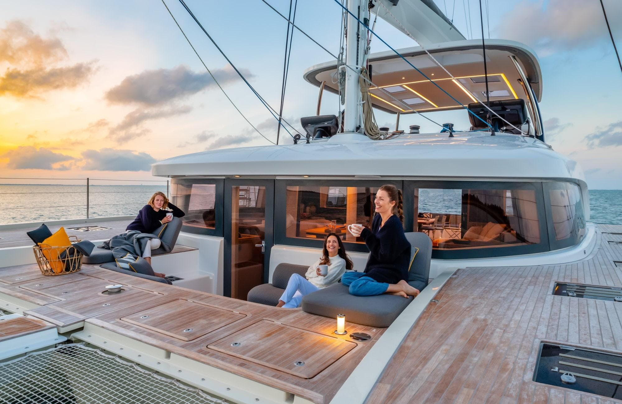 Luxury Lagoon 65 yacht, 2026 model, with people relaxing on deck at sunset.
