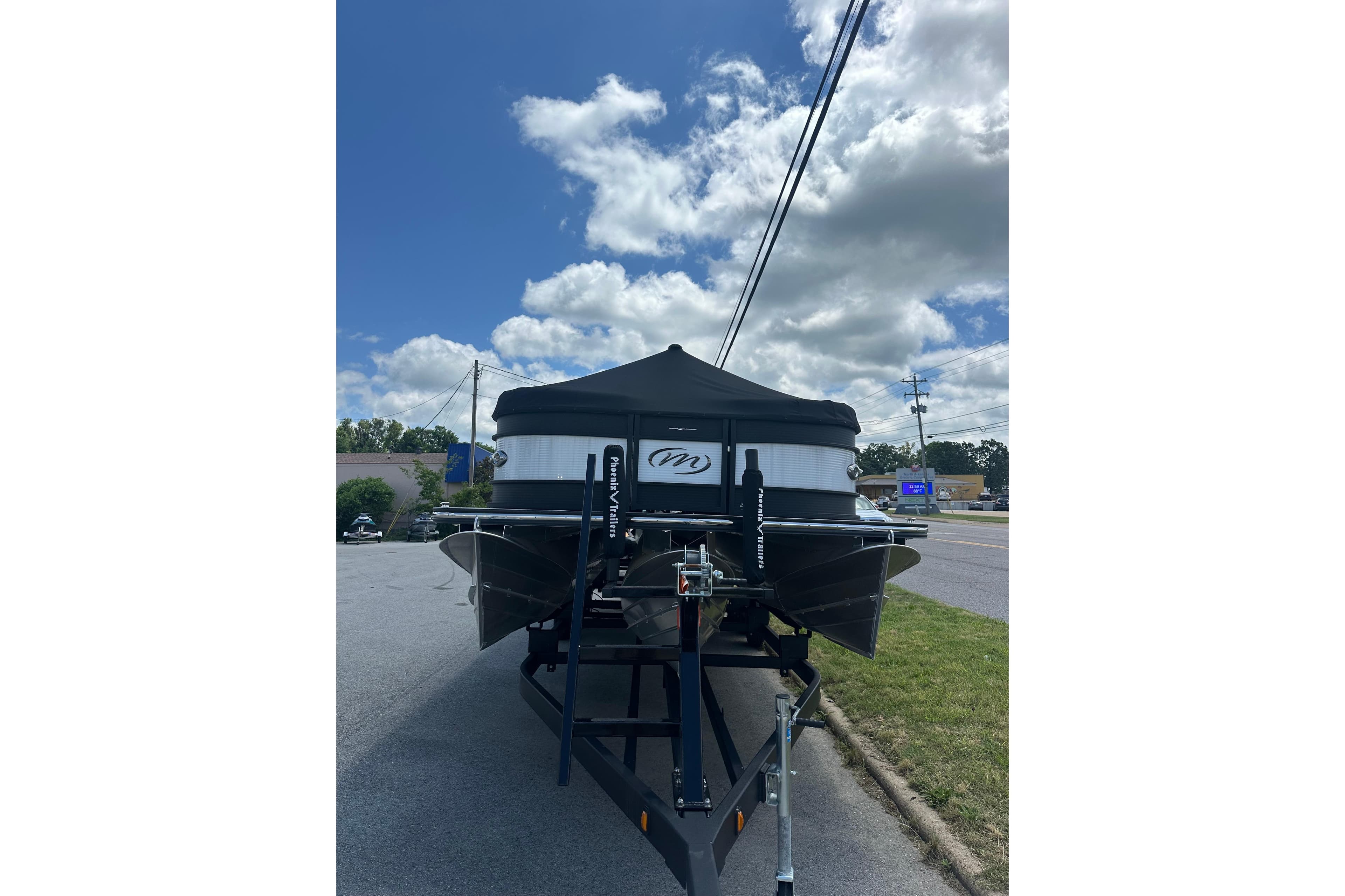 2025 Manitou 25 LX SRW boat on trailer under a partly cloudy sky.