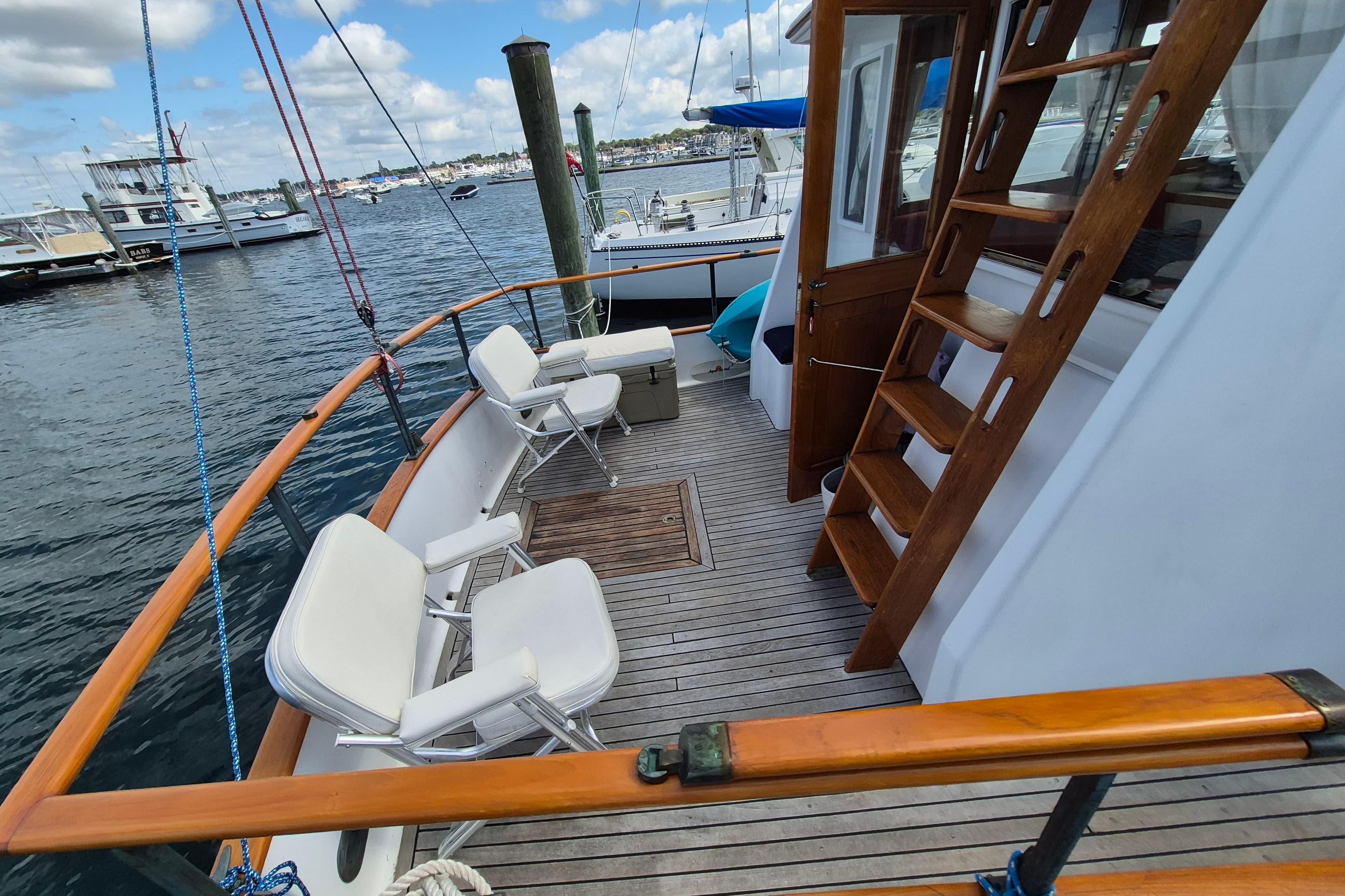 1986 Island Gypsy 32 Sedan Trawler deck with seating and wooden stairs, docked at marina.