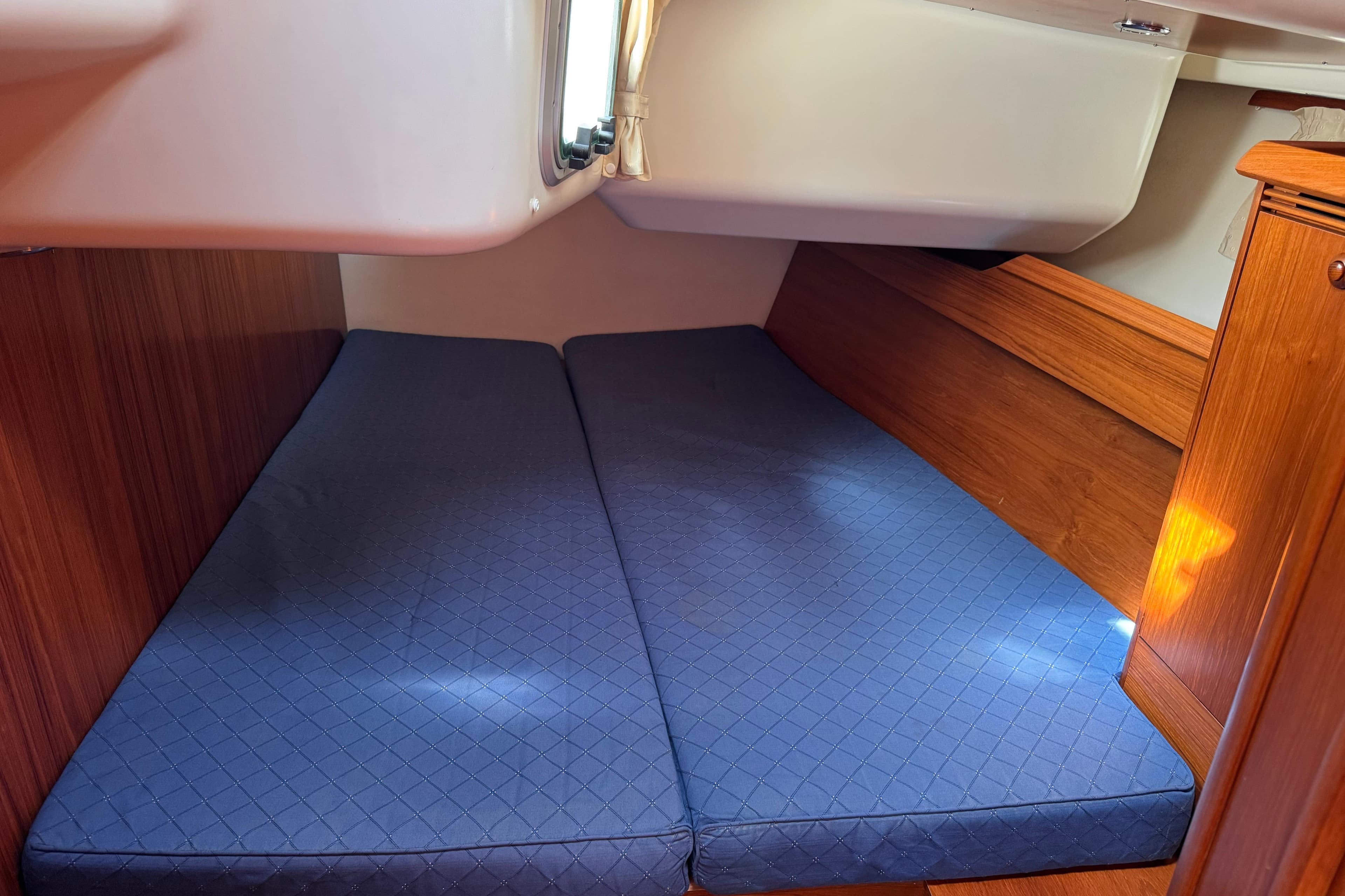 Interior cabin of 2006 Jeanneau Sun Odyssey 45 with blue mattress and wooden finish.