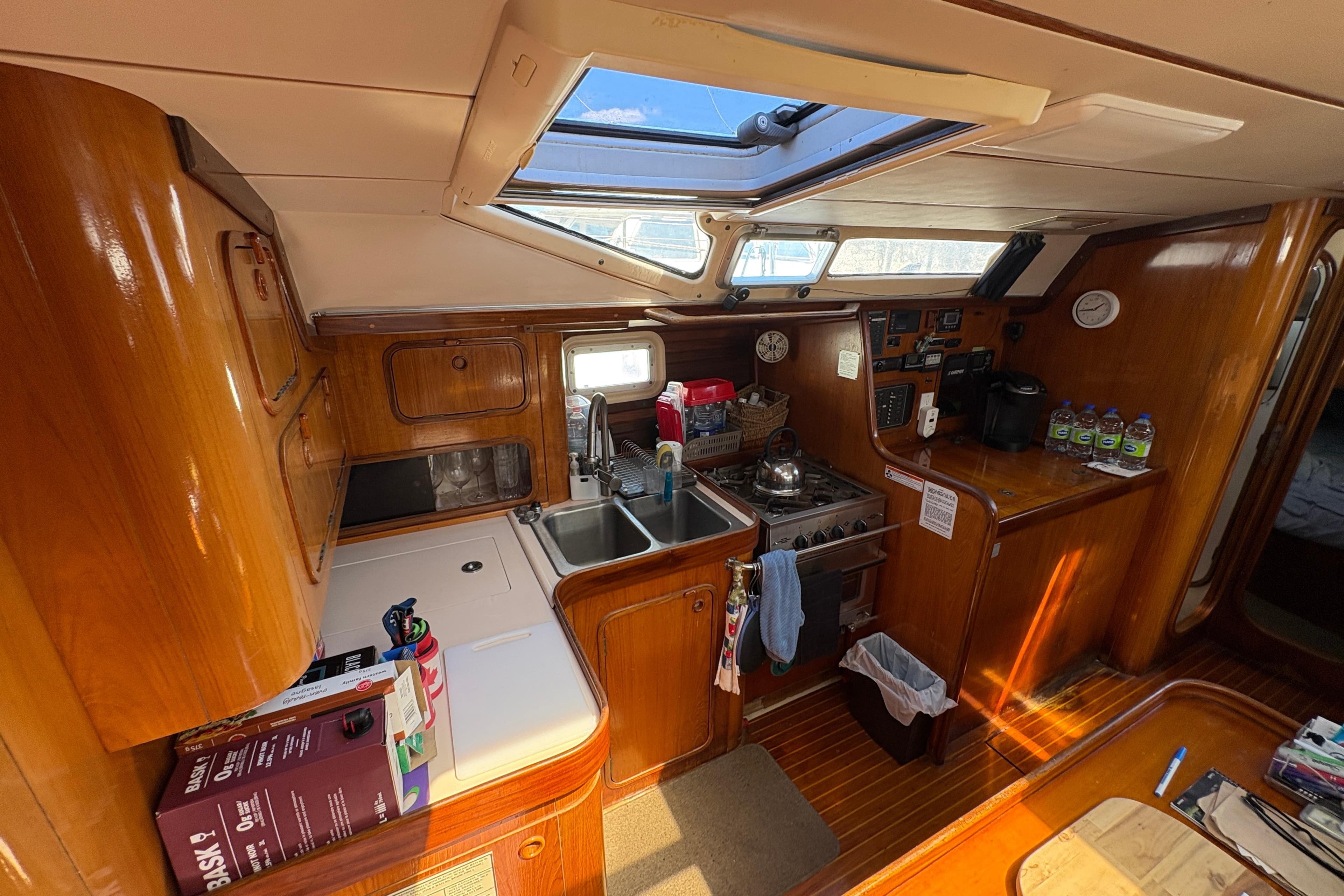 Interior of 1990 Beneteau Oceanis 500 yacht kitchen with wooden cabinetry and skylight.
