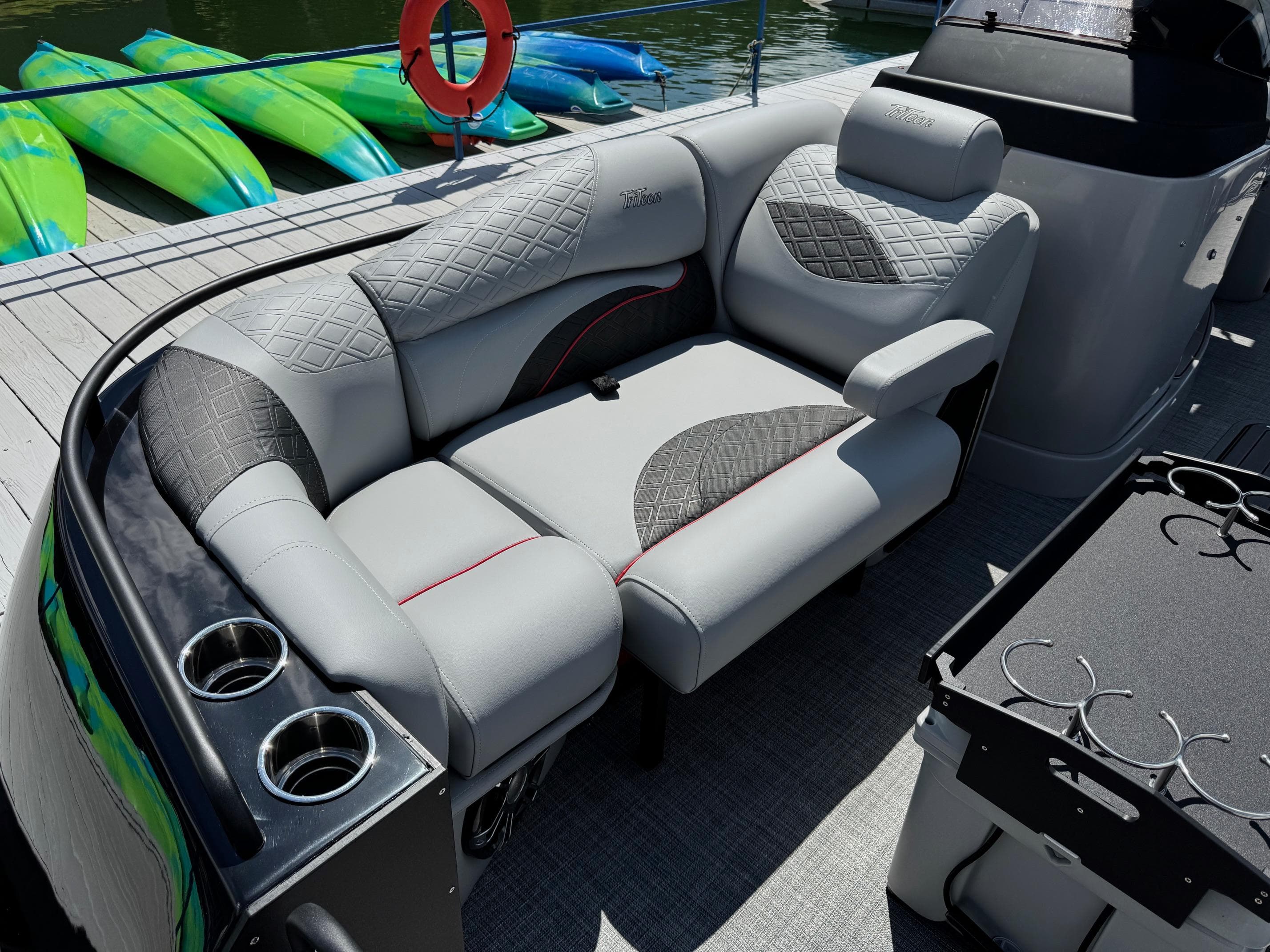 Luxurious seating on 2026 JC SportToon 24 TT DSL pontoon boat, docked with kayaks nearby.