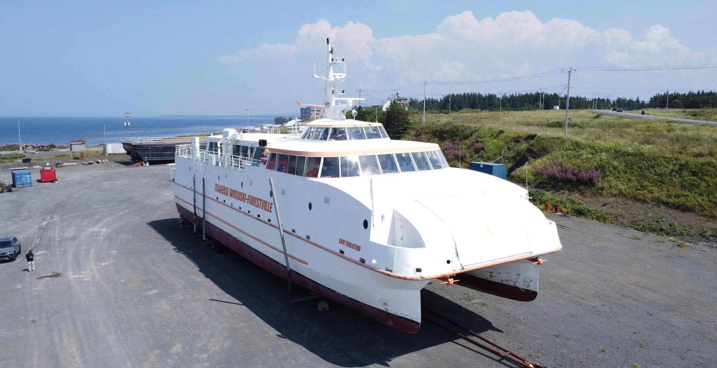 Large white CNM Evolution catamaran from 1997 on dry land near the coast.