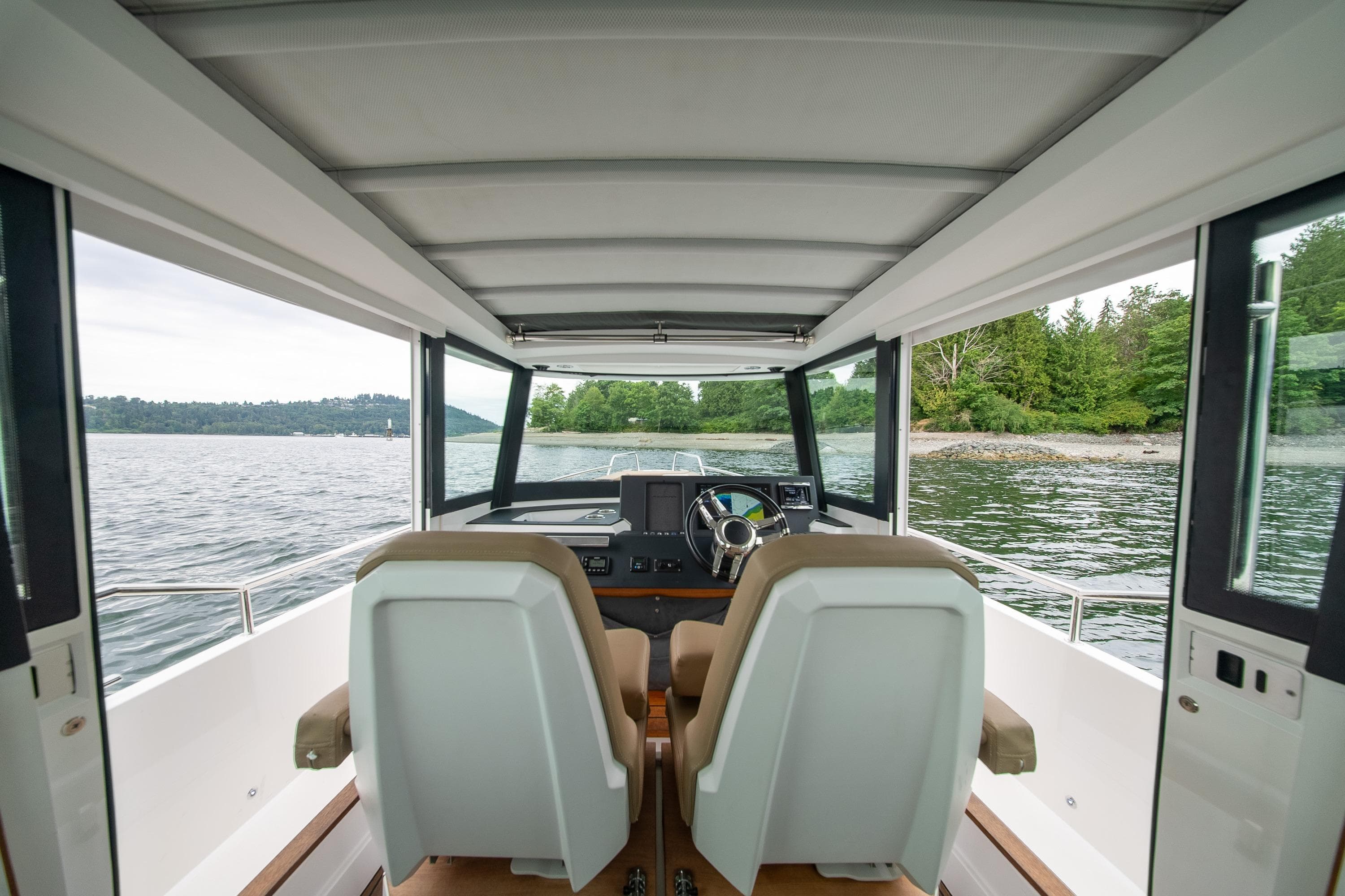 Interior view of 2016 Axopar 28 Cabin boat with scenic water and forest backdrop.
