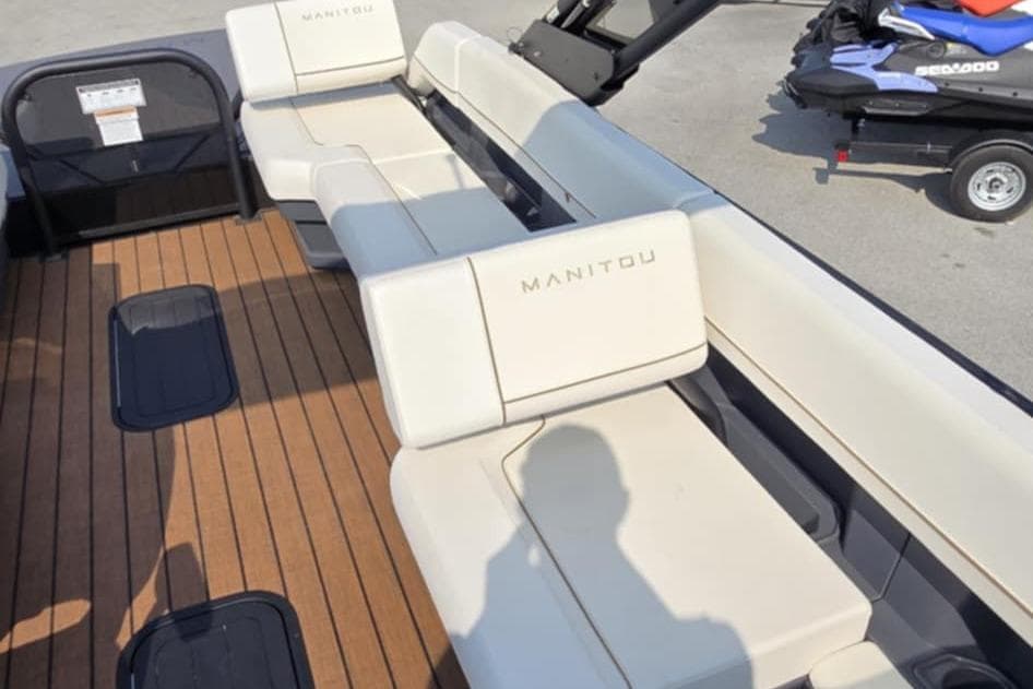 2025 Manitou Explore boat interior with beige seating and wooden deck.