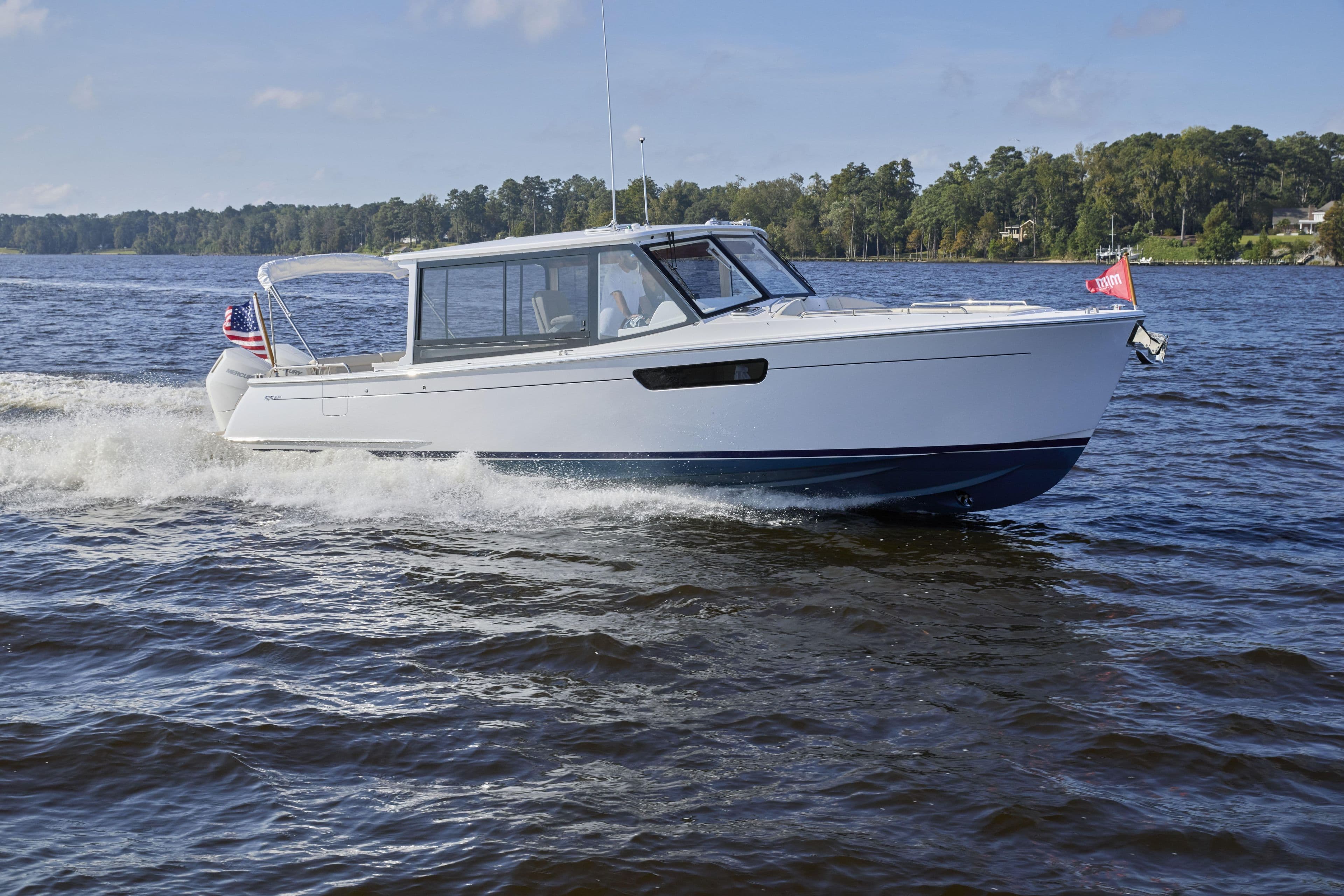 2026 MJM 38 X boat cruising on a scenic lake under a clear blue sky.