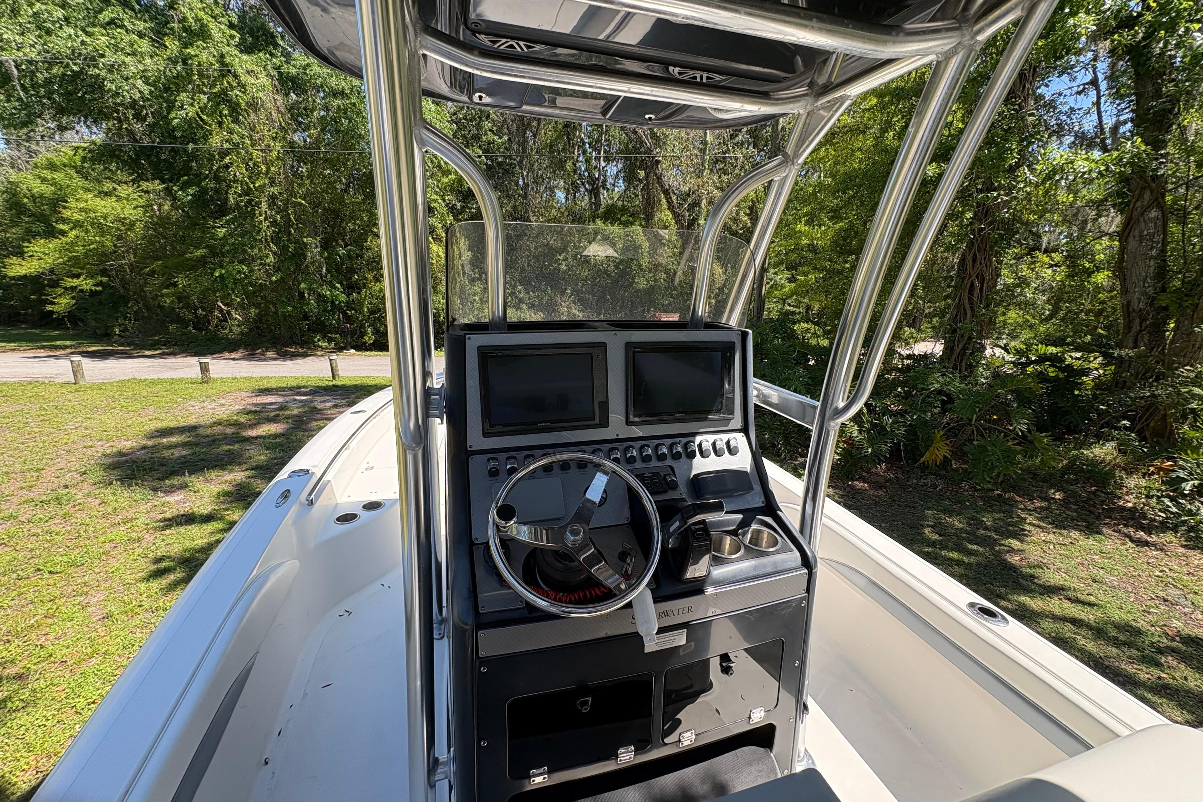 2018 ShearWater 26 Carolina boat console with dual screens and steering wheel, surrounded by greenery.