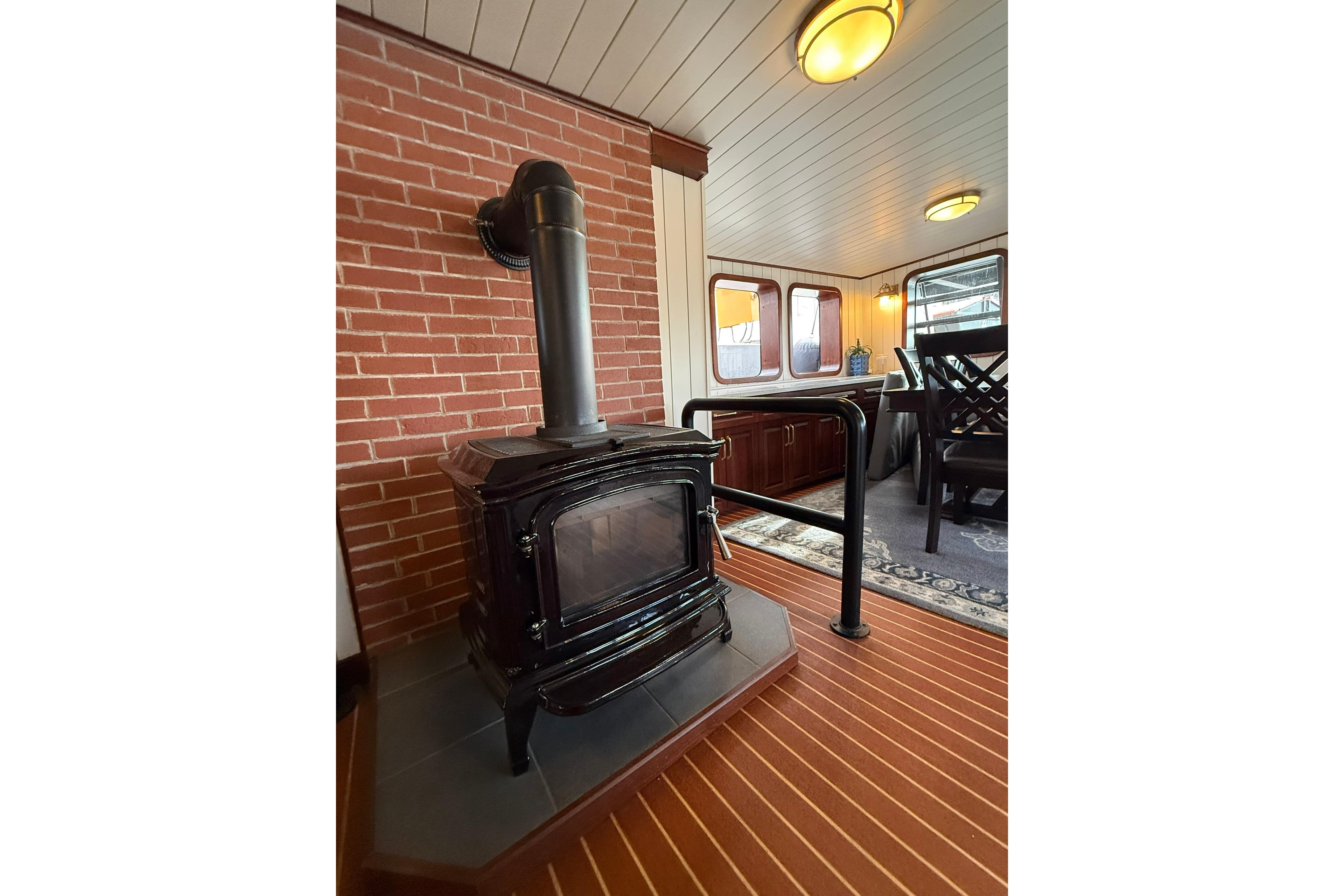Cozy ship interior with wood stove, brick wall, and dining area, Custom Glovertown Shipyard 2021.