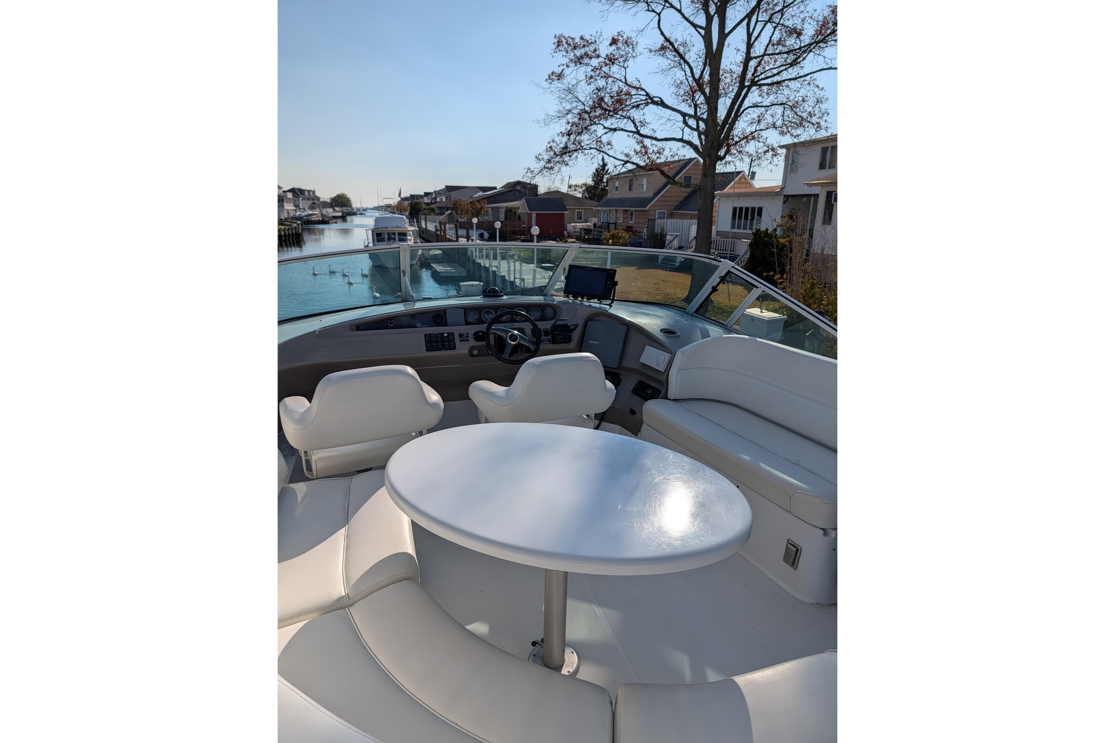 1999 Carver 450 Voyager Pilothouse yacht interior with seating and table, docked by waterfront homes.